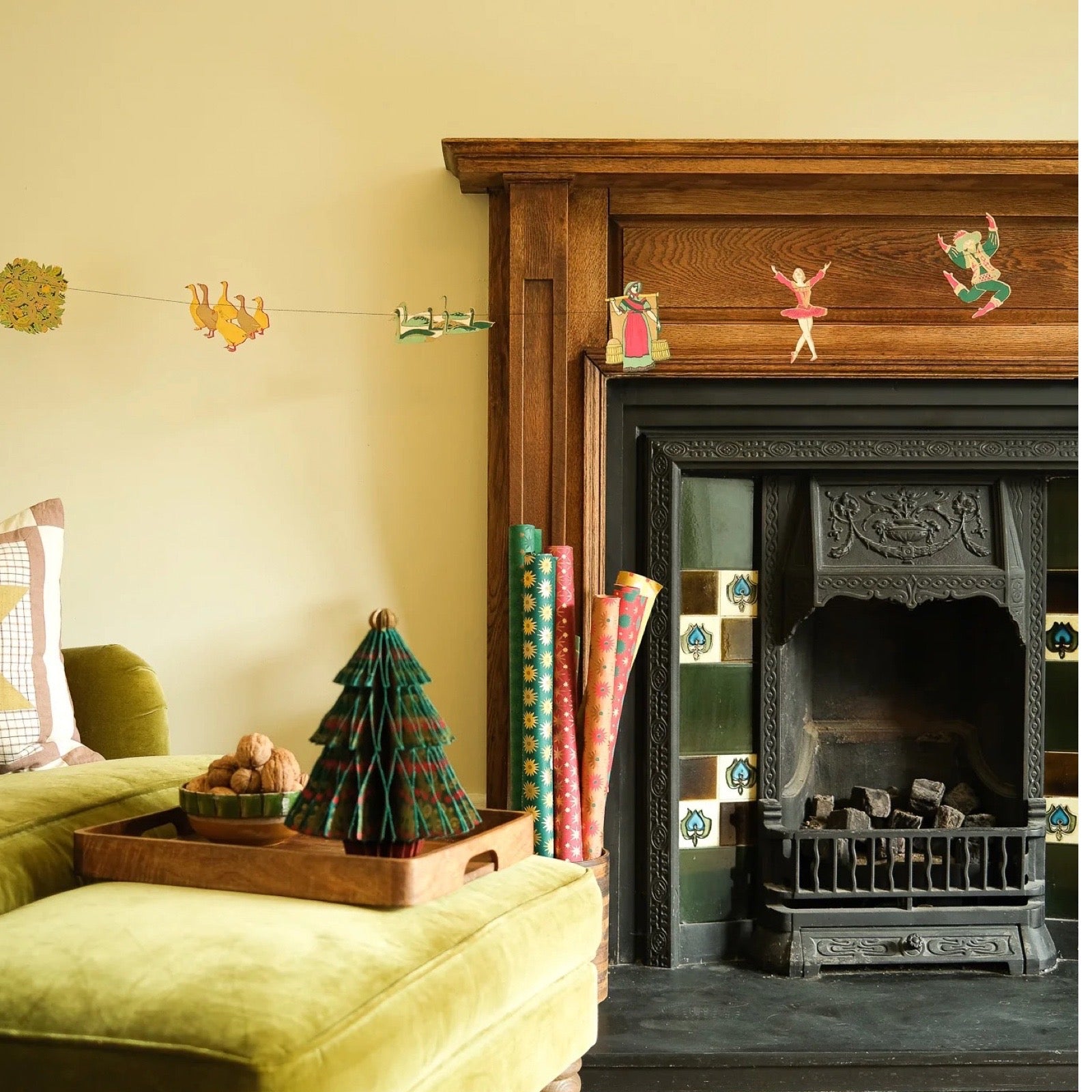 Decorative mantel with small figurines above a fireplace, surrounded by decorations and a decorative tree on a sofa.