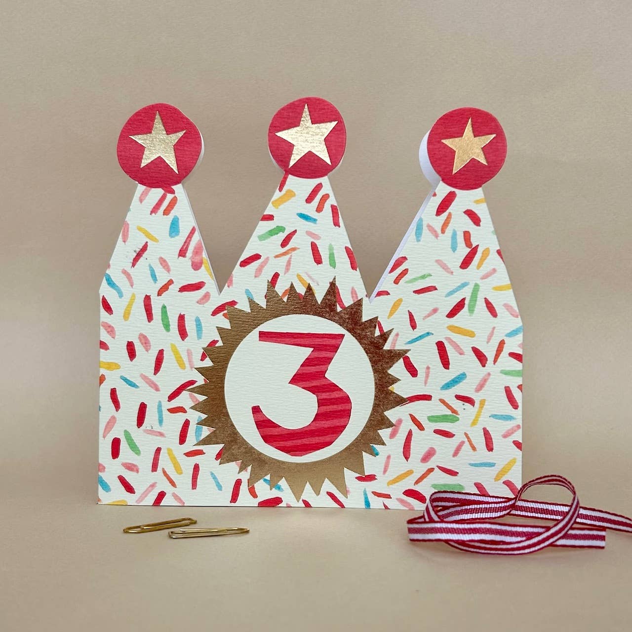 Three colourful birthday hats with a number 3 design on a beige background.
