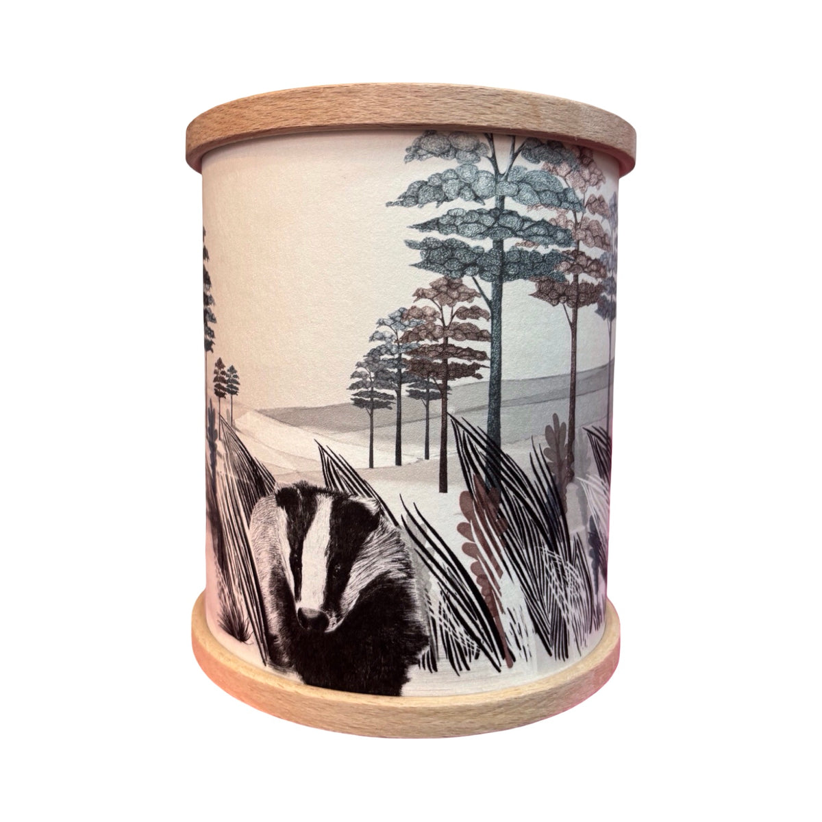 A cylindrical candle holder with a light wood rim and base, featuring an illustration of a badger among trees and reeds.