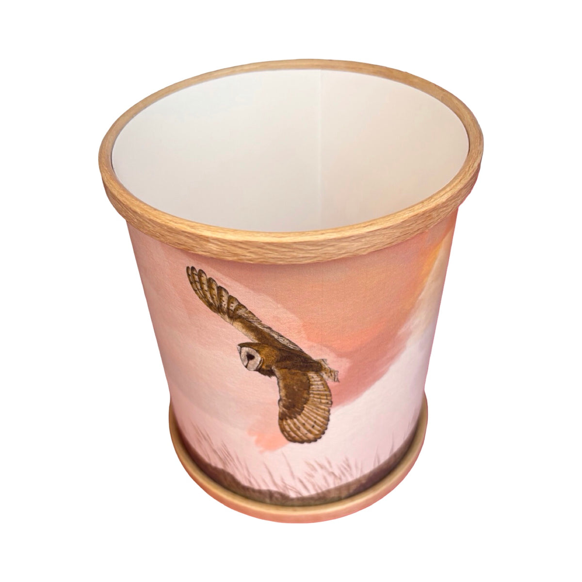 A cylindrical candle holder with a light wood-look rim and base, featuring a printed illustration of a barn owl in flight against a soft pink and peach sky background.