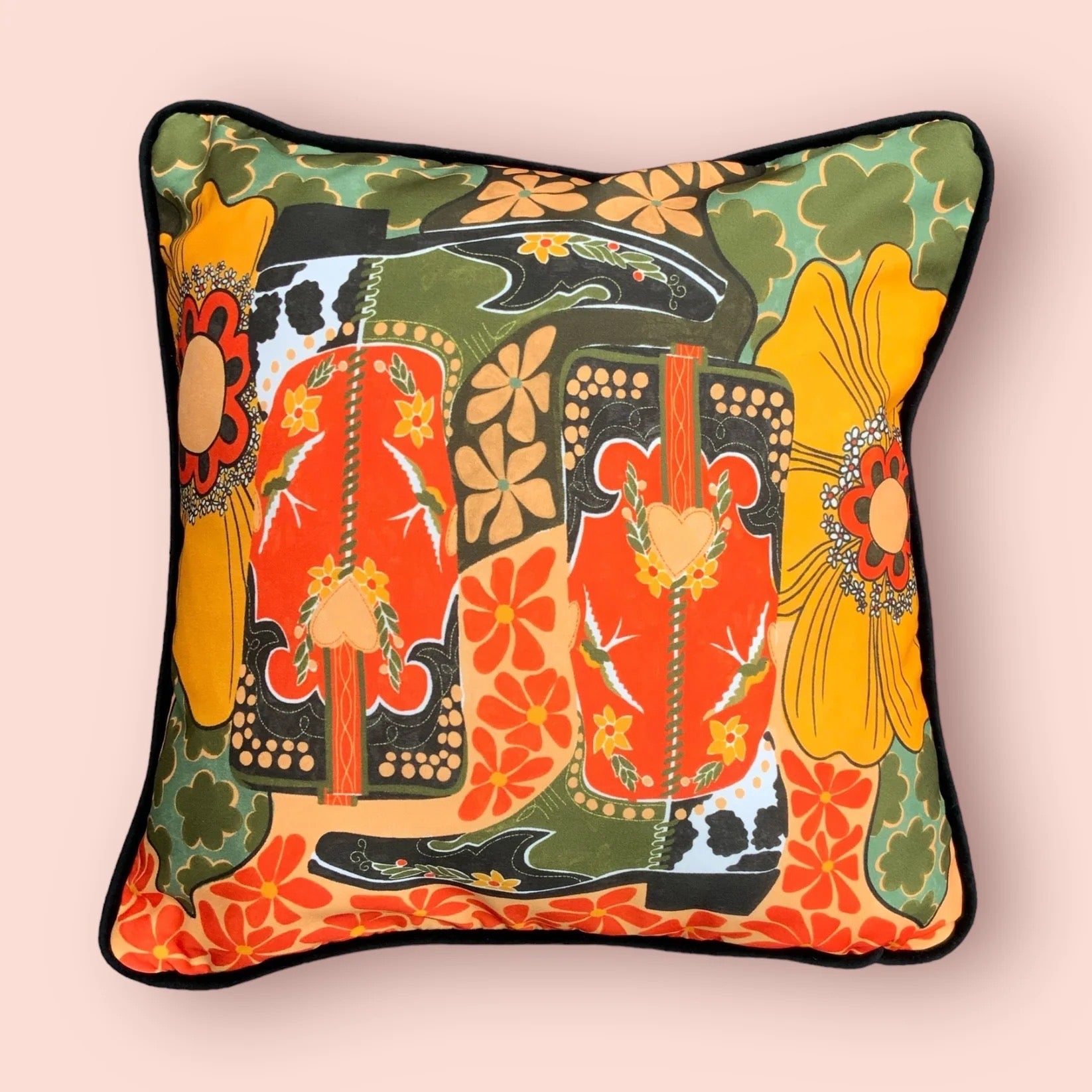 A cushion cover featuring a pair of cowboy boots surrounded by flowers, all in retro tones, on a pink background.