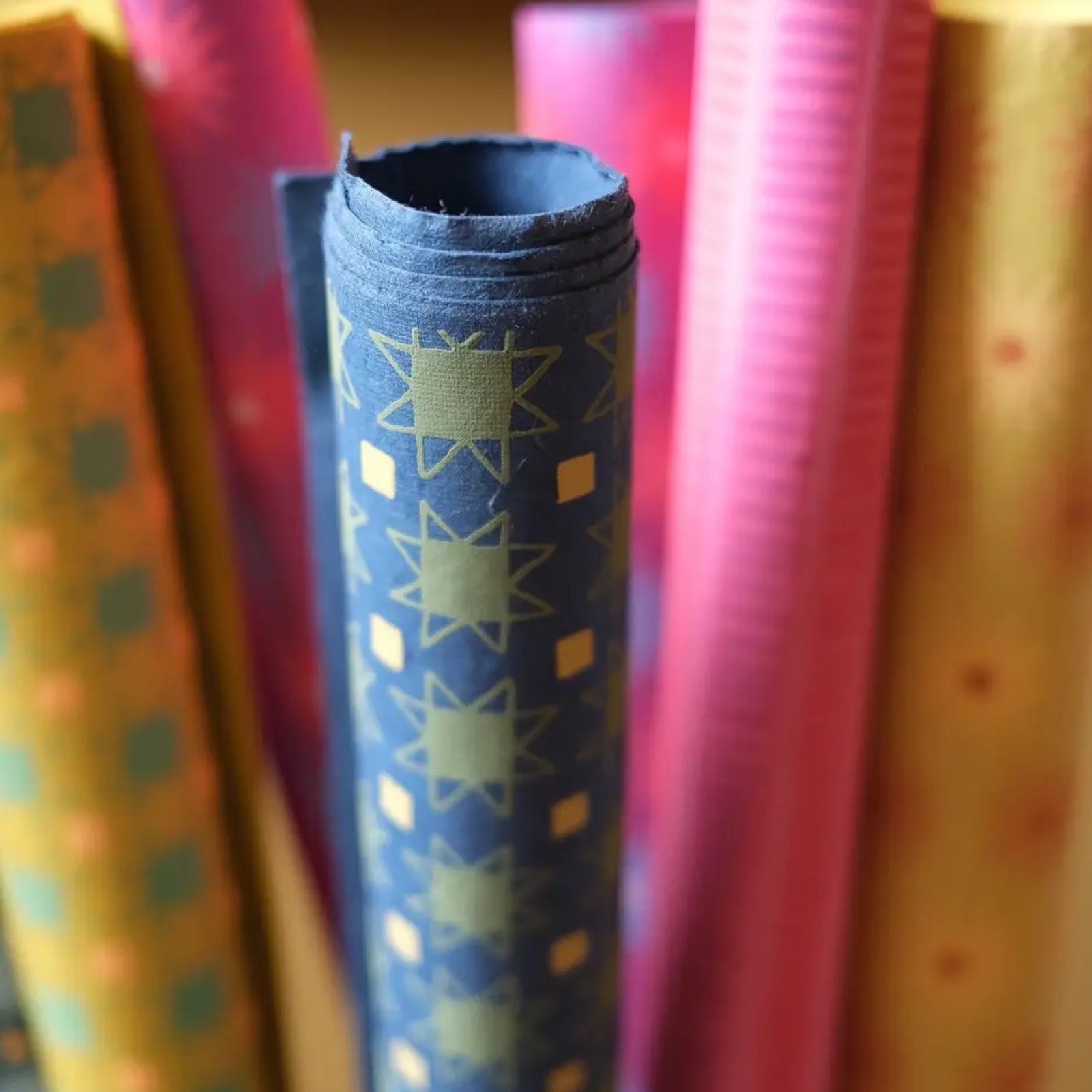 A roll of wrapping paper with green stars and yellow squares against a blue background.