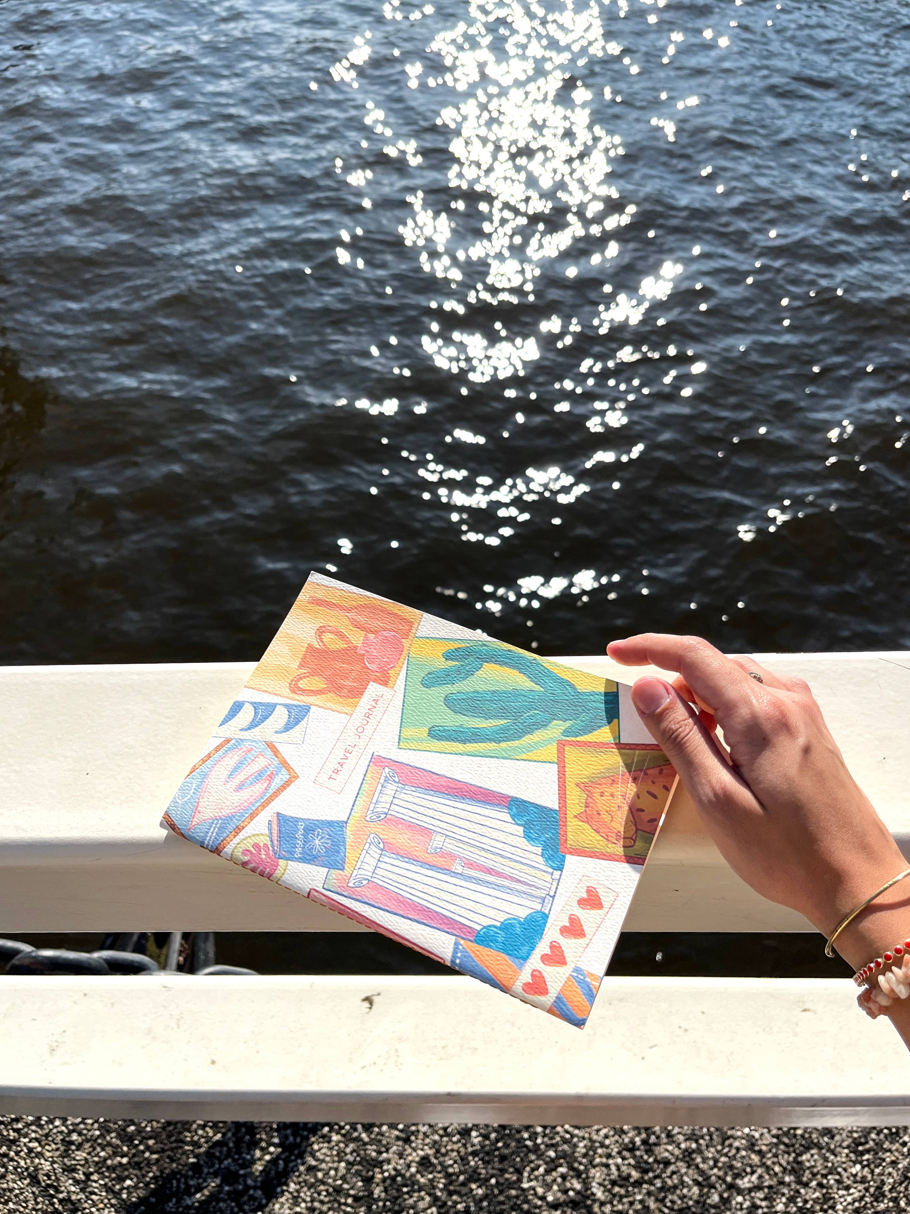 Colorful travel journal held by a hand by a body of water.