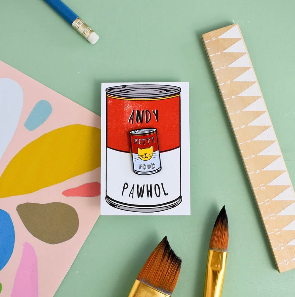 Pin with a red can design featuring 'Andy Pawhol' on a colorful background with paint tools.