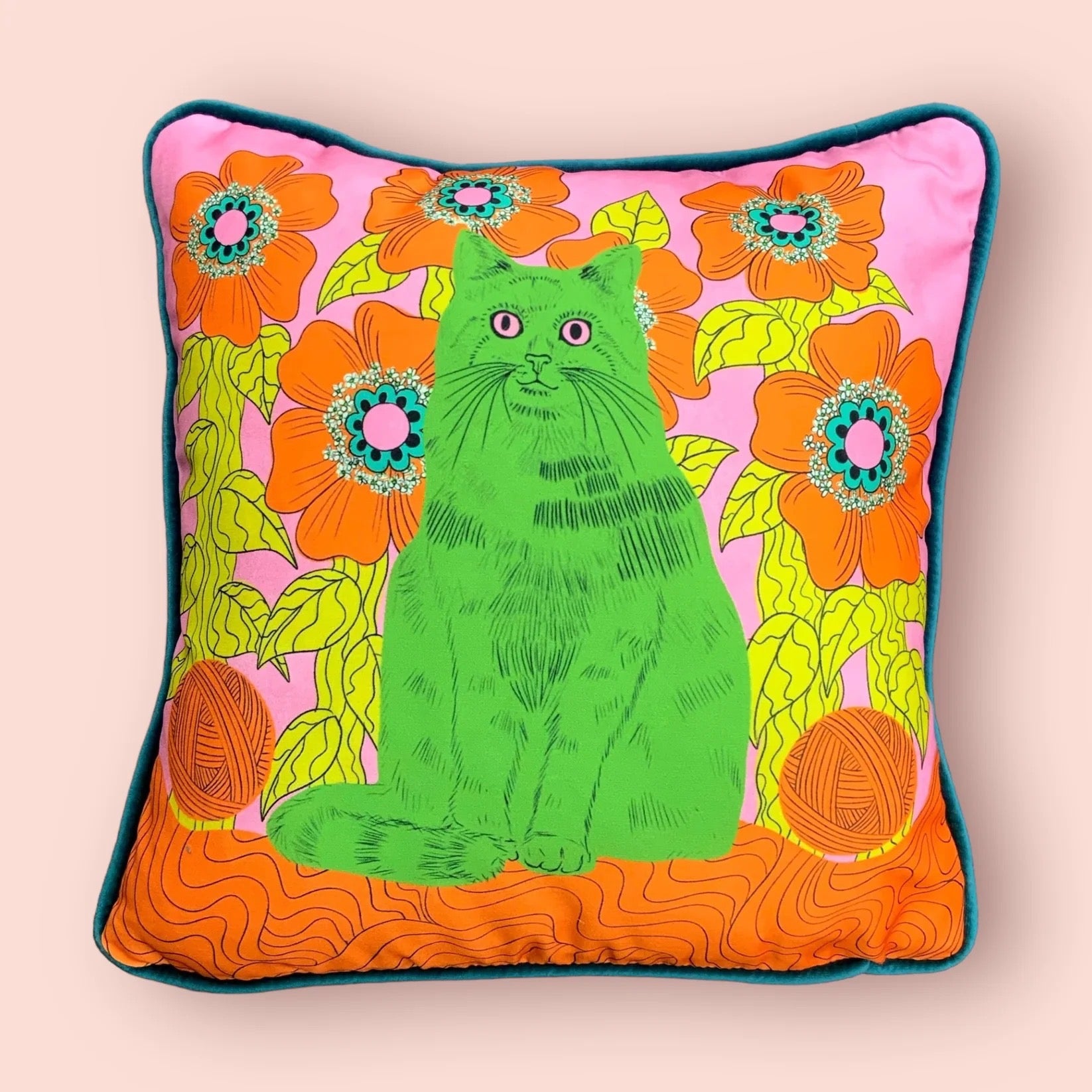Colourful cushion with a green cat and floral design on a pink background.