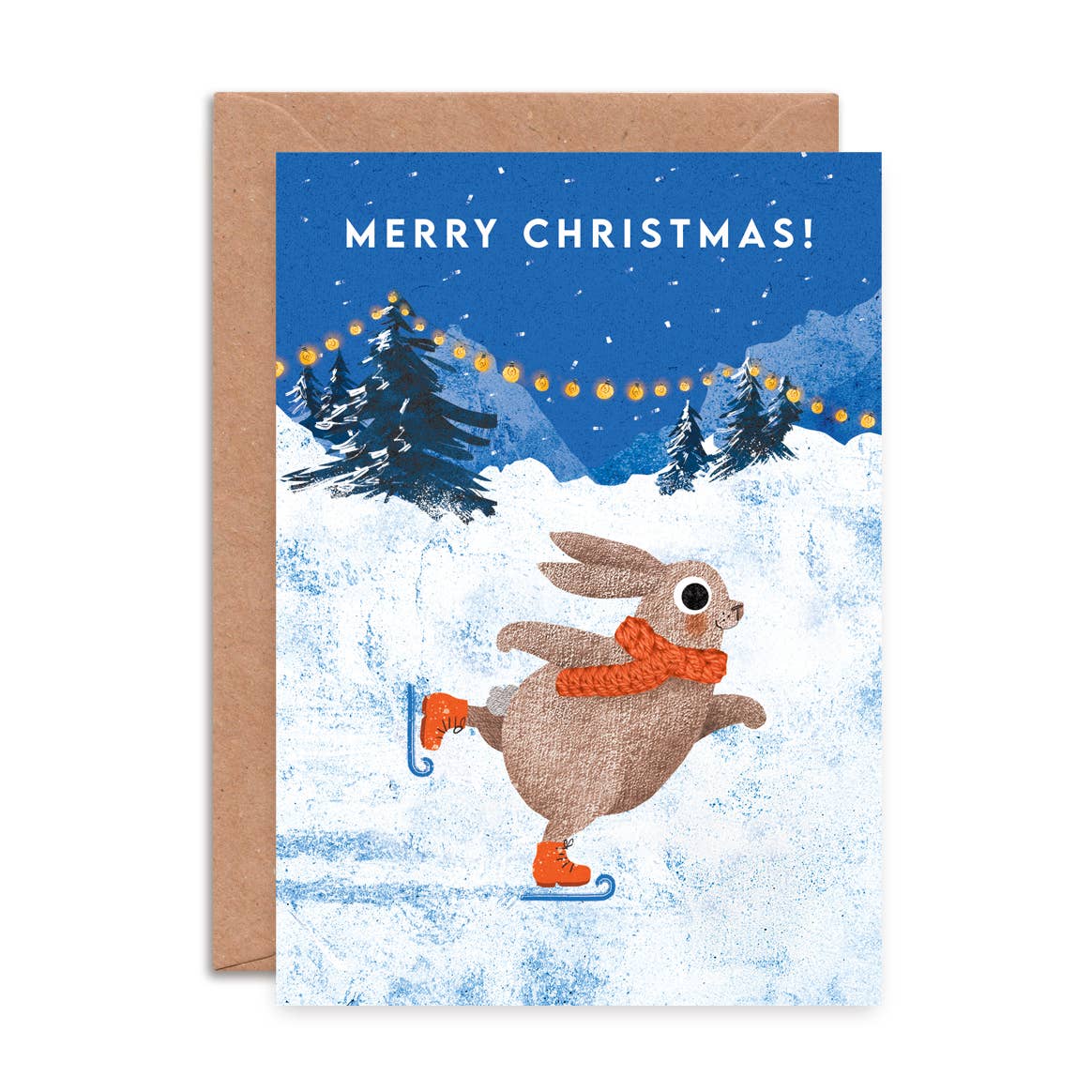 A Christmas greeting card with a kraft envelope behind it. The card features an illustration of a brown rabbit ice skating in the snow, wearing an orange scarf and orange boots, under a blue night sky with the text 'MERRY CHRISTMAS!'.