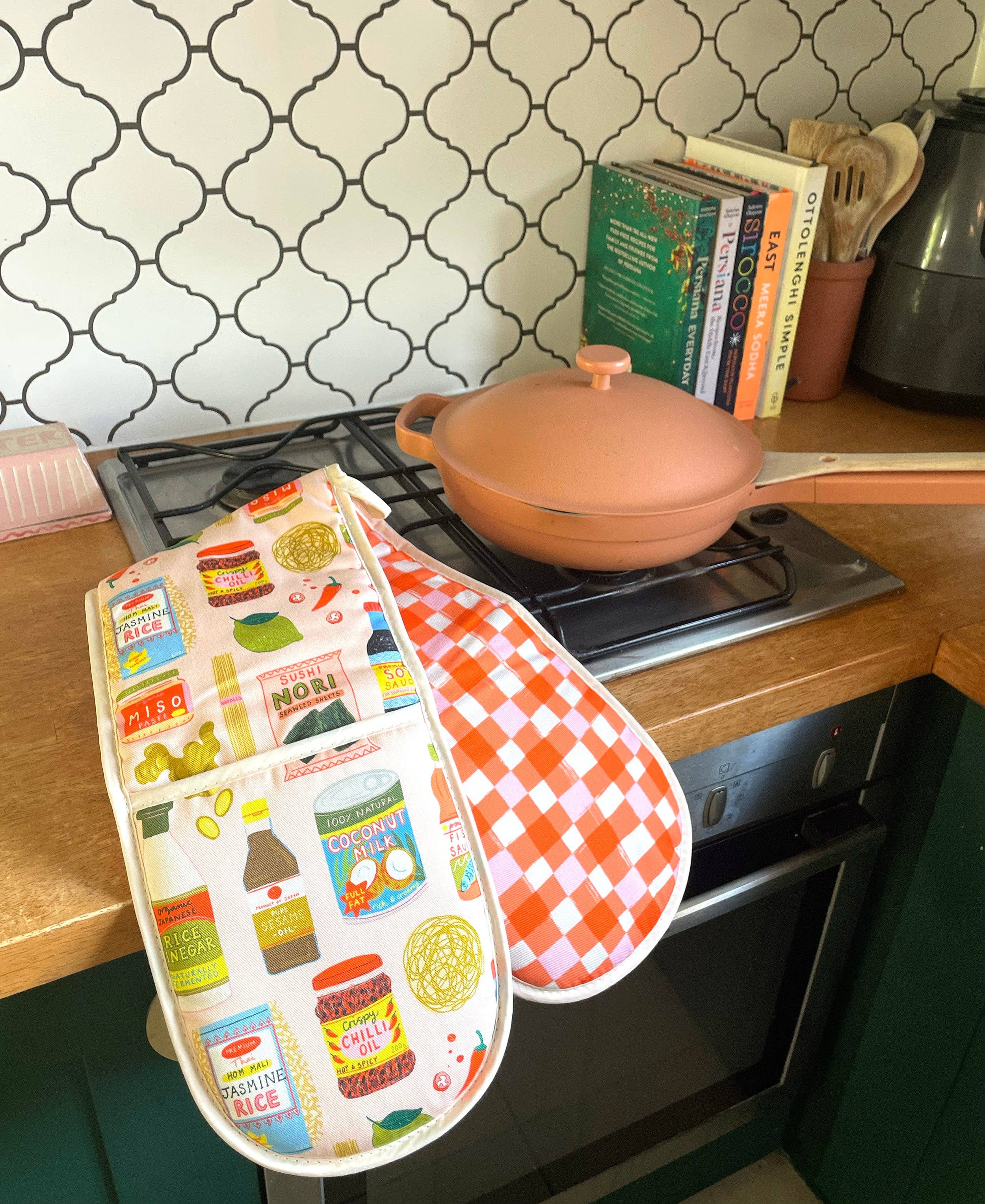 Oven mitt with food-themed design hanging on a stove in a kitchen.