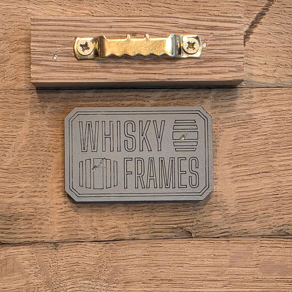 Metallic 'Whisky Frames' logo on a wooden background.