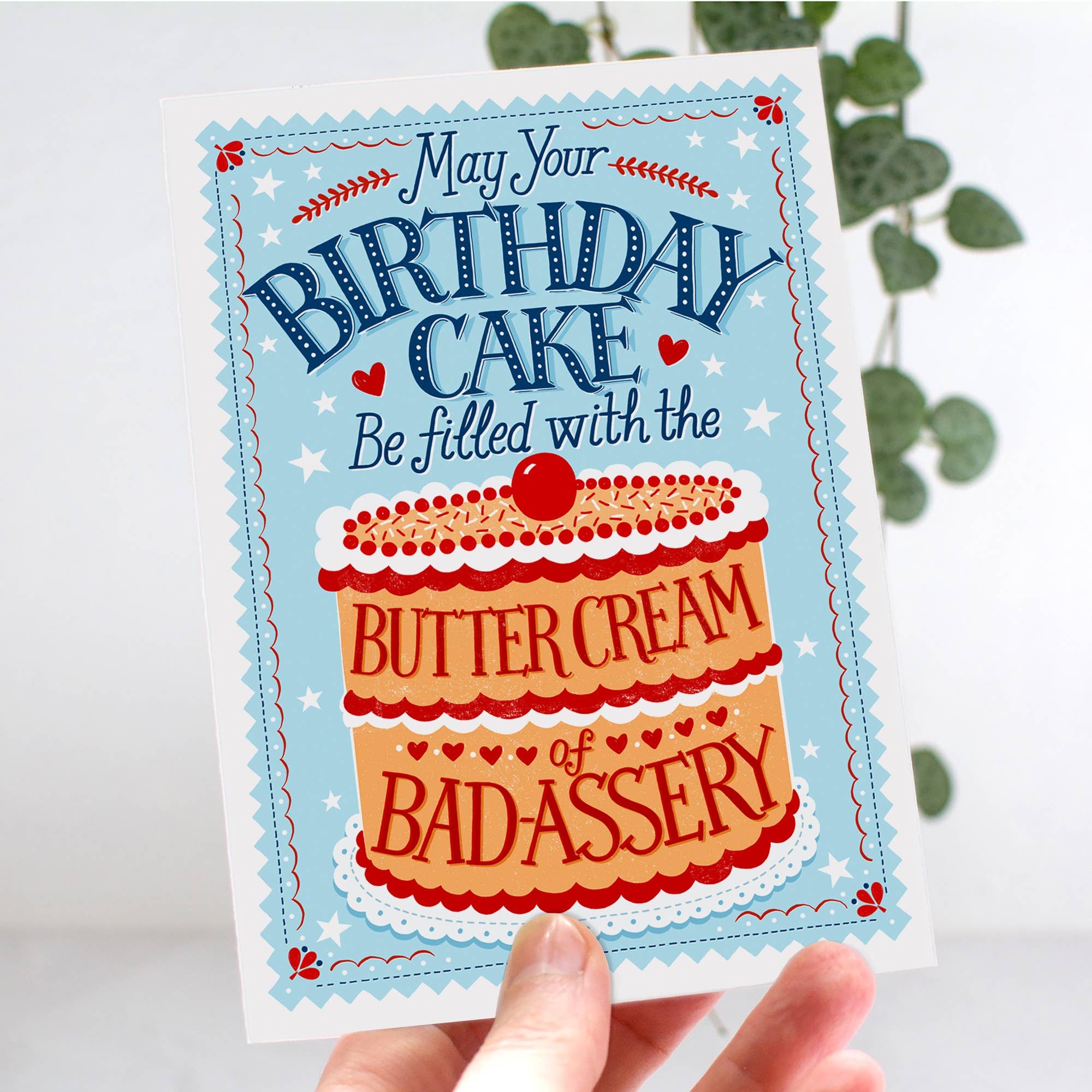 Birthday card with cake illustration and humorous text held by a hand.