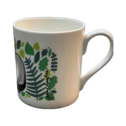 A white fine bone china mug featuring an illustration of a black and white badger surrounded by green leaves.