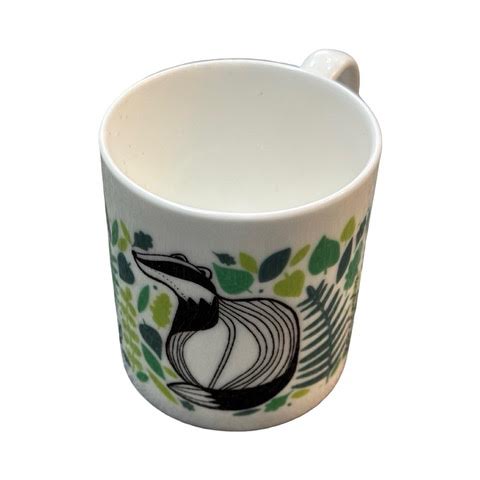 A white fine bone china mug featuring an illustration of a black and white badger surrounded by green leaves.