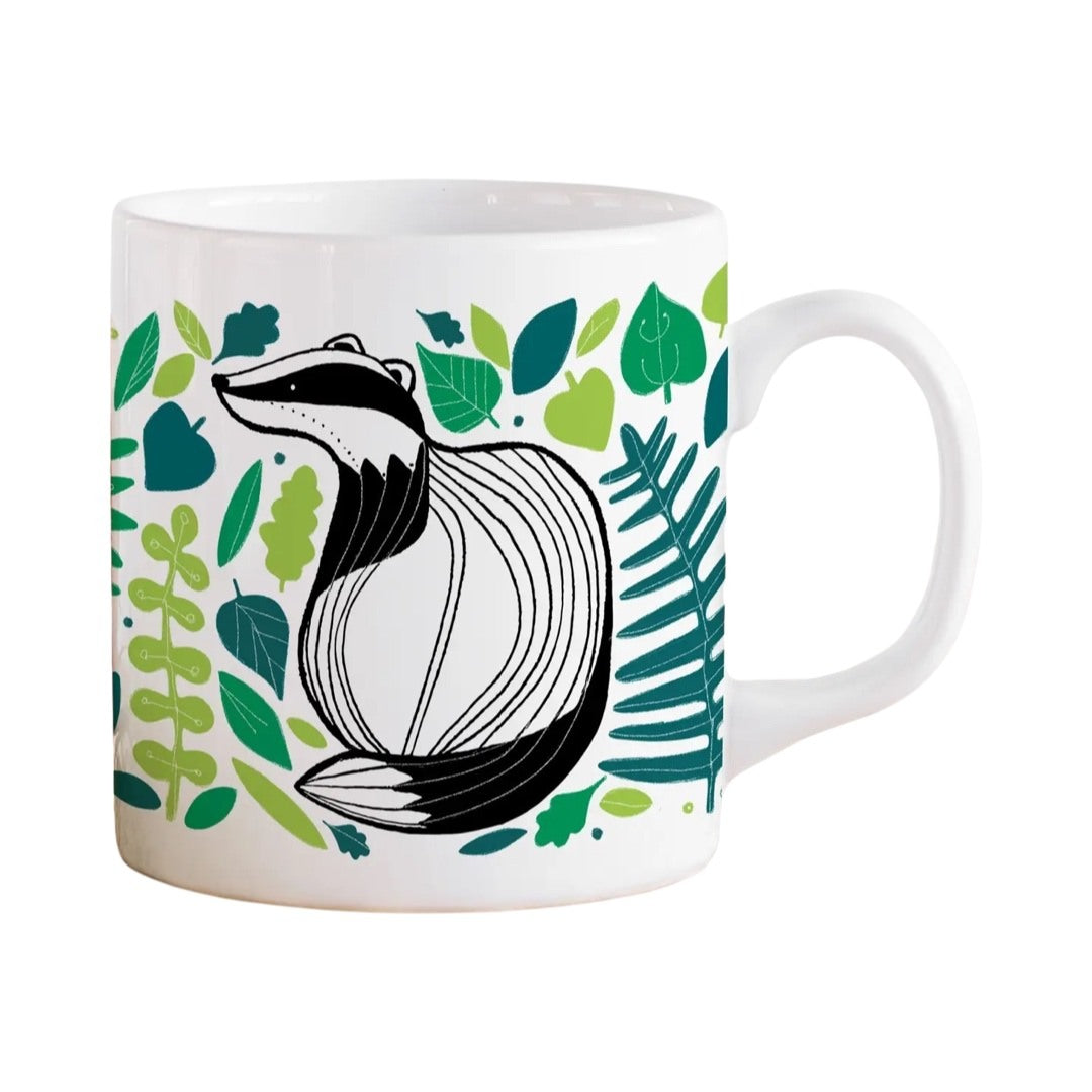 A white fine bone china mug featuring an illustration of a black and white badger surrounded by green leaves.