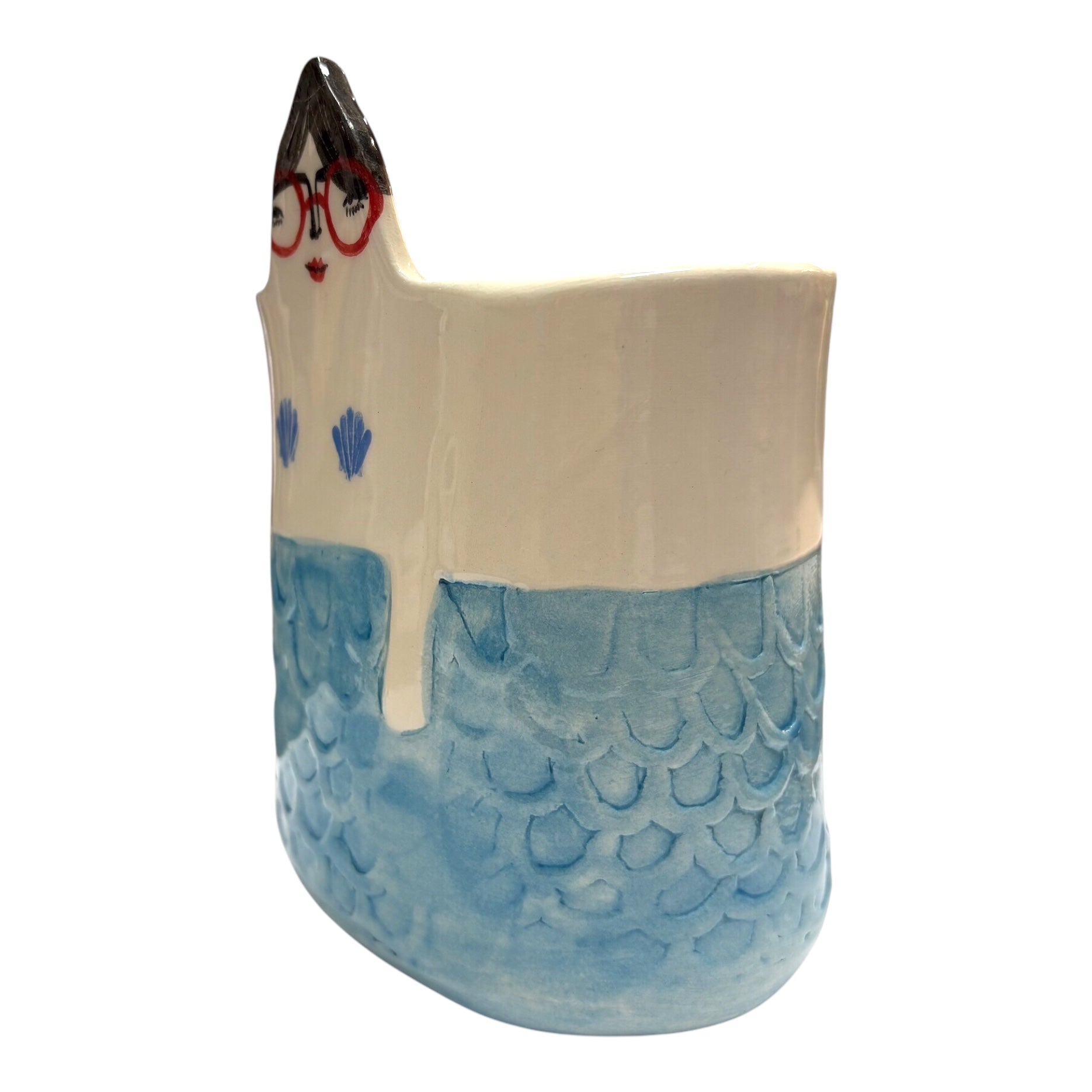 The side of a handmade ceramic pot with teal mermaid scales and a lady's head with dark hair and red glasses.