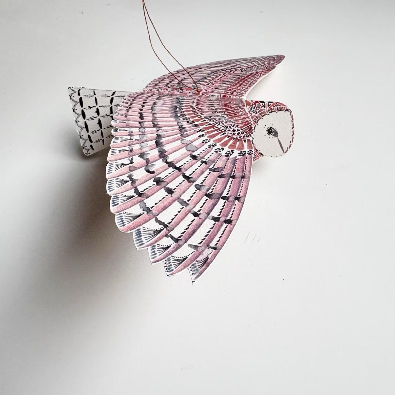 Decorative owl ornament with pink and black feathers on a white background.