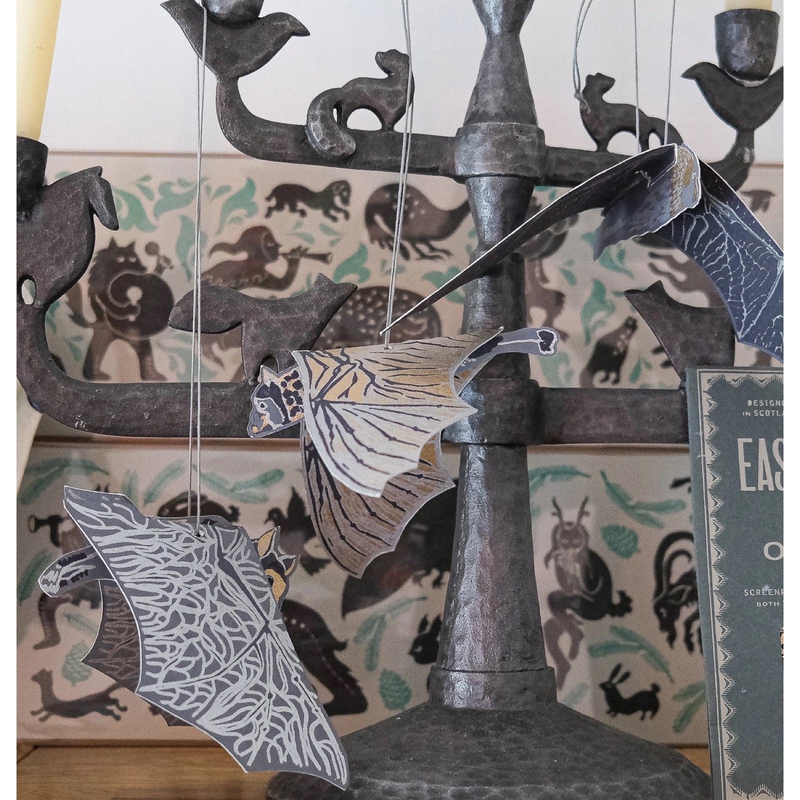 3 recycled paper hanging bat decorations in black, grey and gold hanging on a black vintage gothic candle stick.