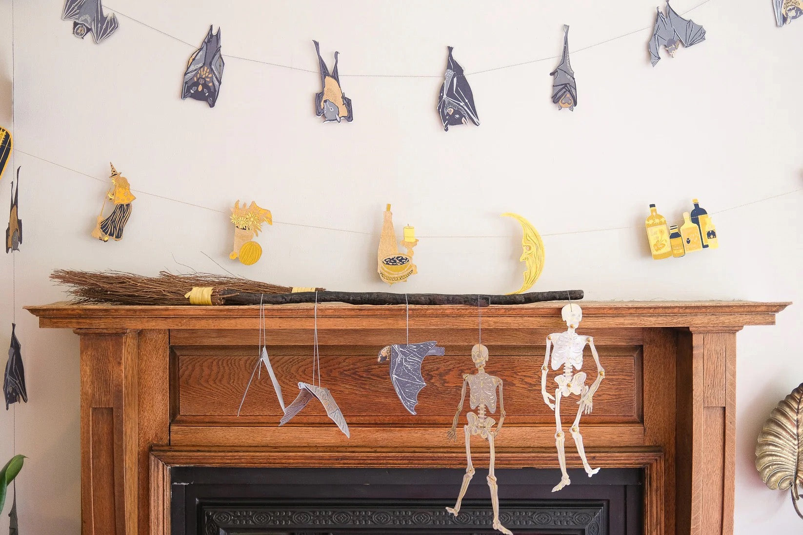 Halloween decorations on a fireplace mantle with skeletons, witches, and bats.