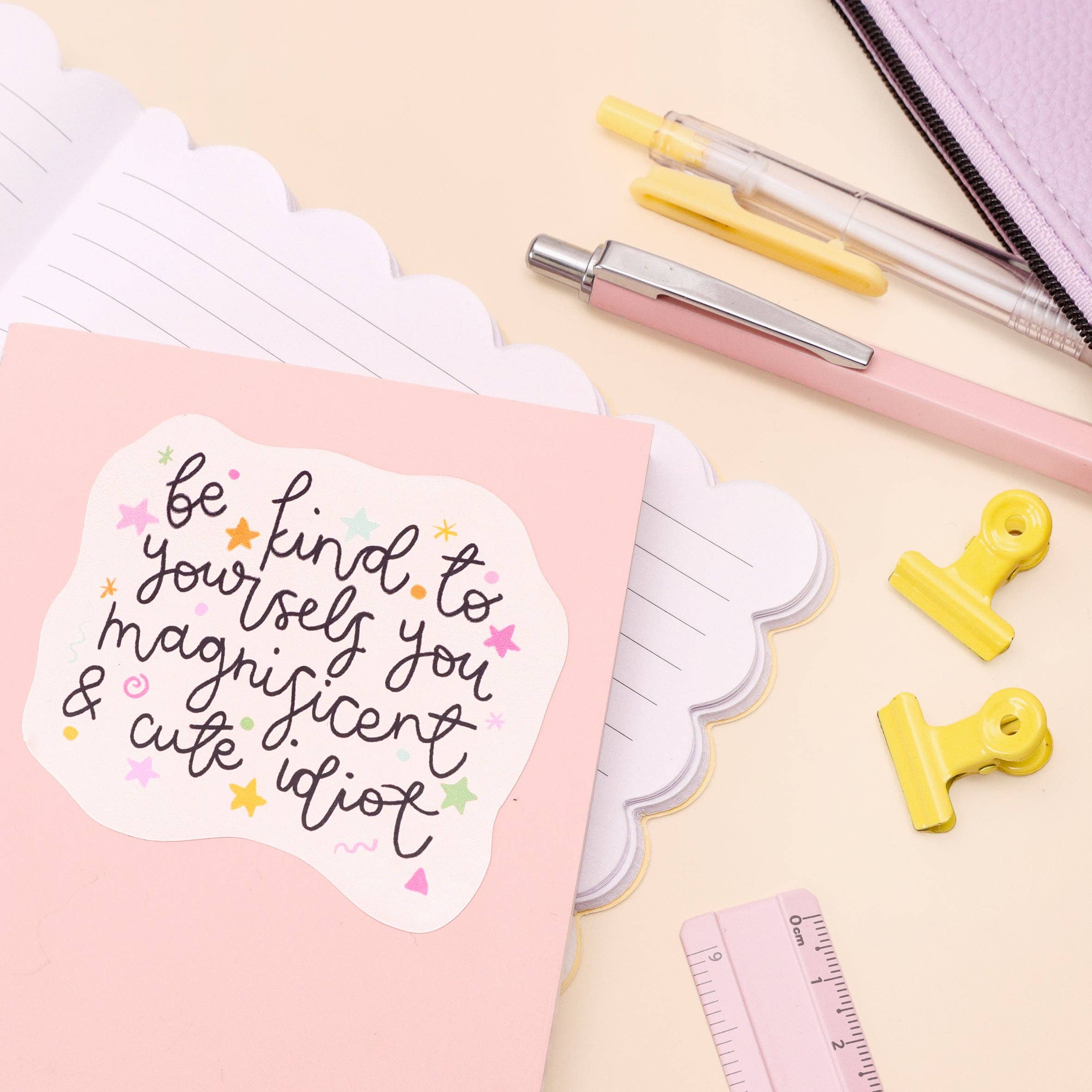 Motivational sticker on a pink notebook with stationery items on a light background.