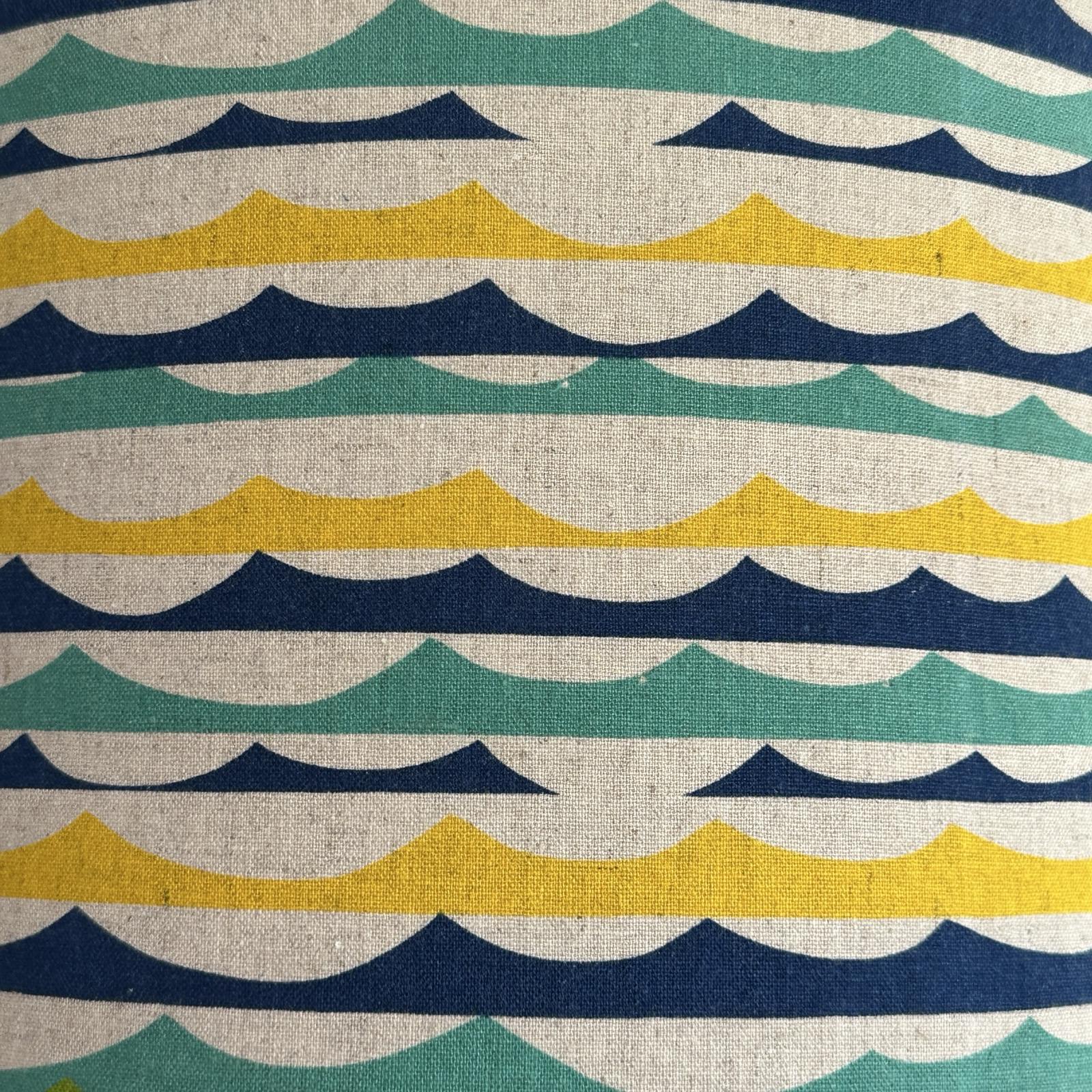 Colourful striped green, blue and yellow beach wave lampshade on a white background.