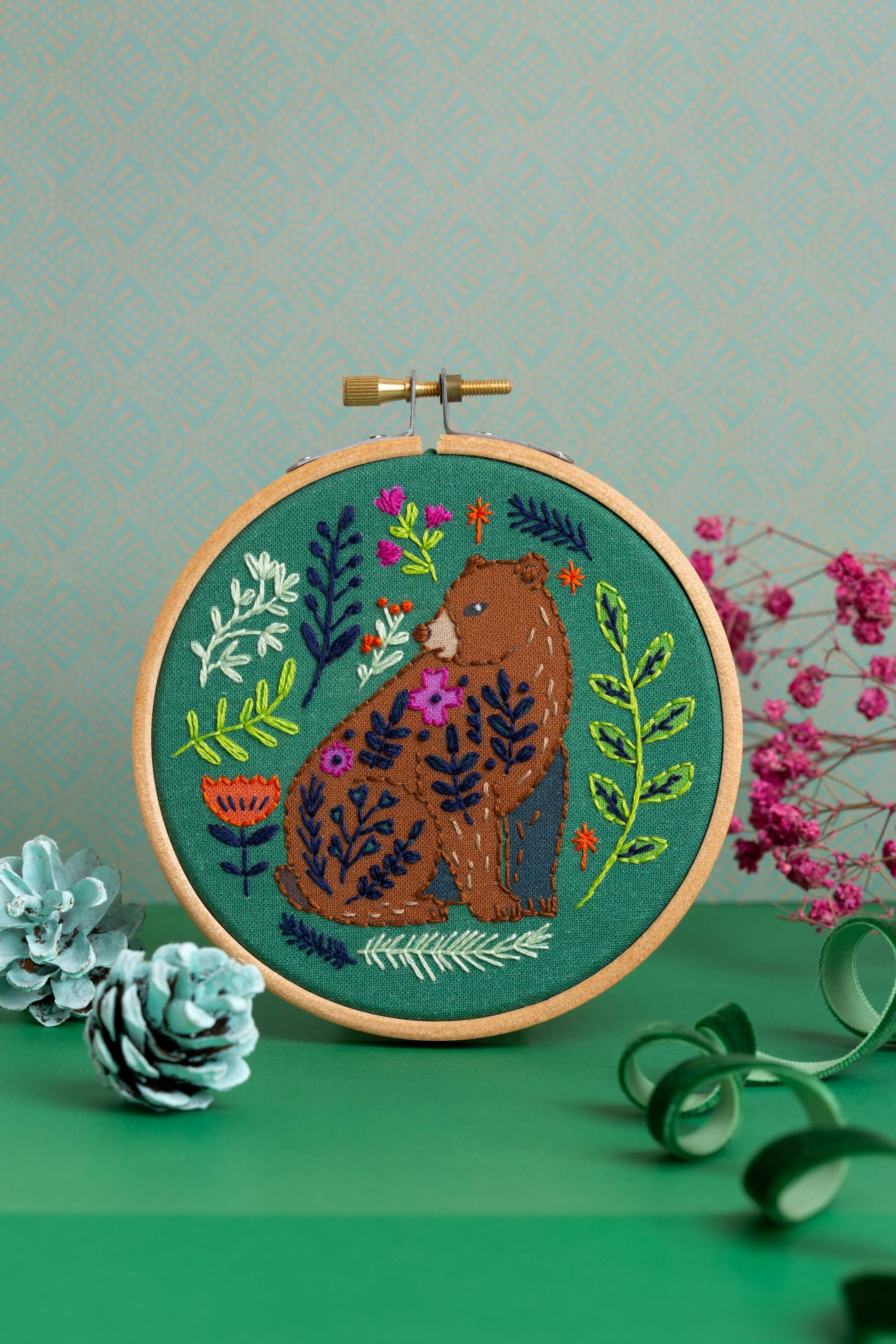 Embroidery hoop with a bear design surrounded by flowers and leaves on a green background