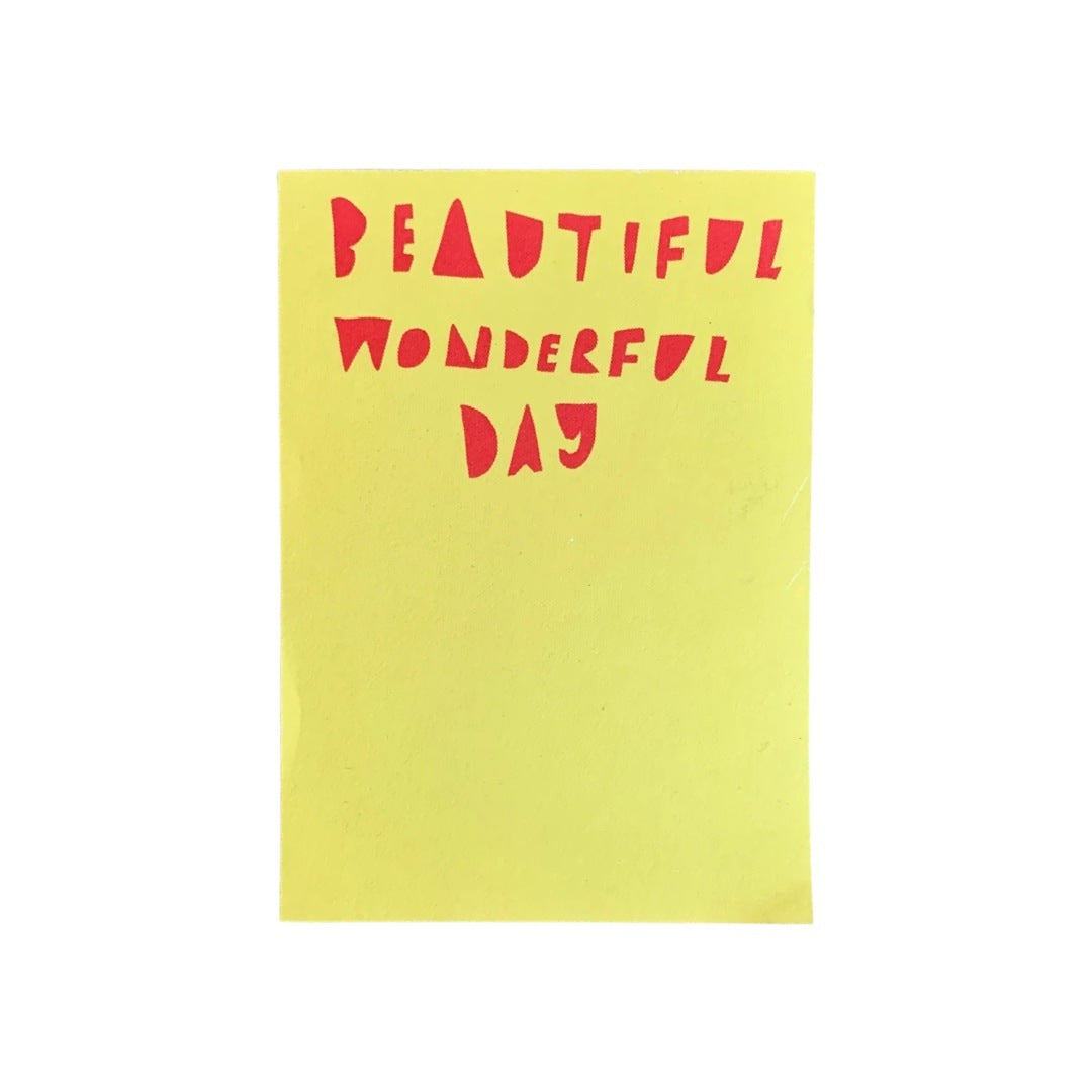 A yellow A6 notepad with the text 'Beautiful Wonderful Day' written in red.