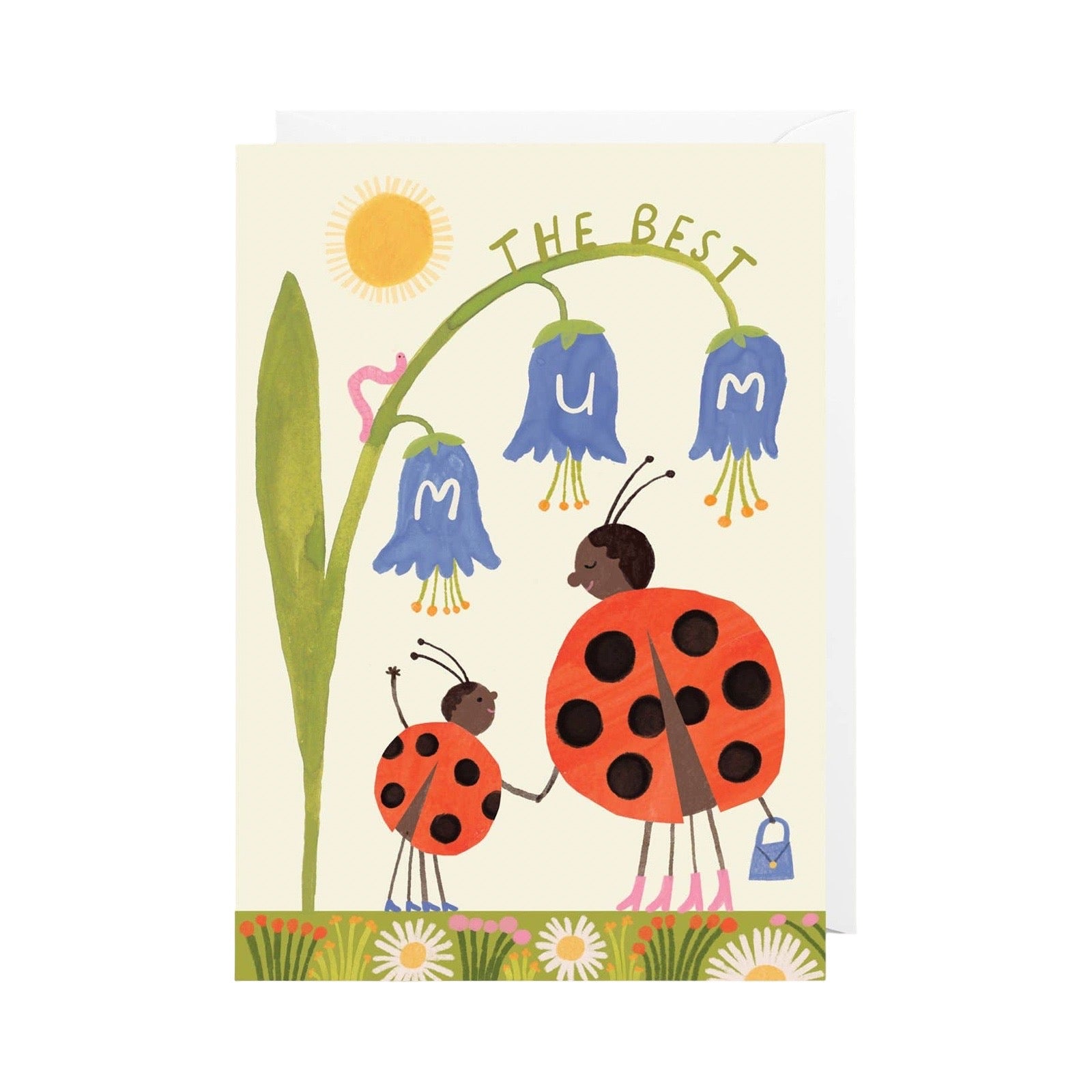 A greeting card featuring a whimsical illustration of two ladybugs standing beside blue bellflowers with the letters M, U, and M, under the words 'THE BEST'. The card is shown standing upright with an envelope behind it on a plain white background.