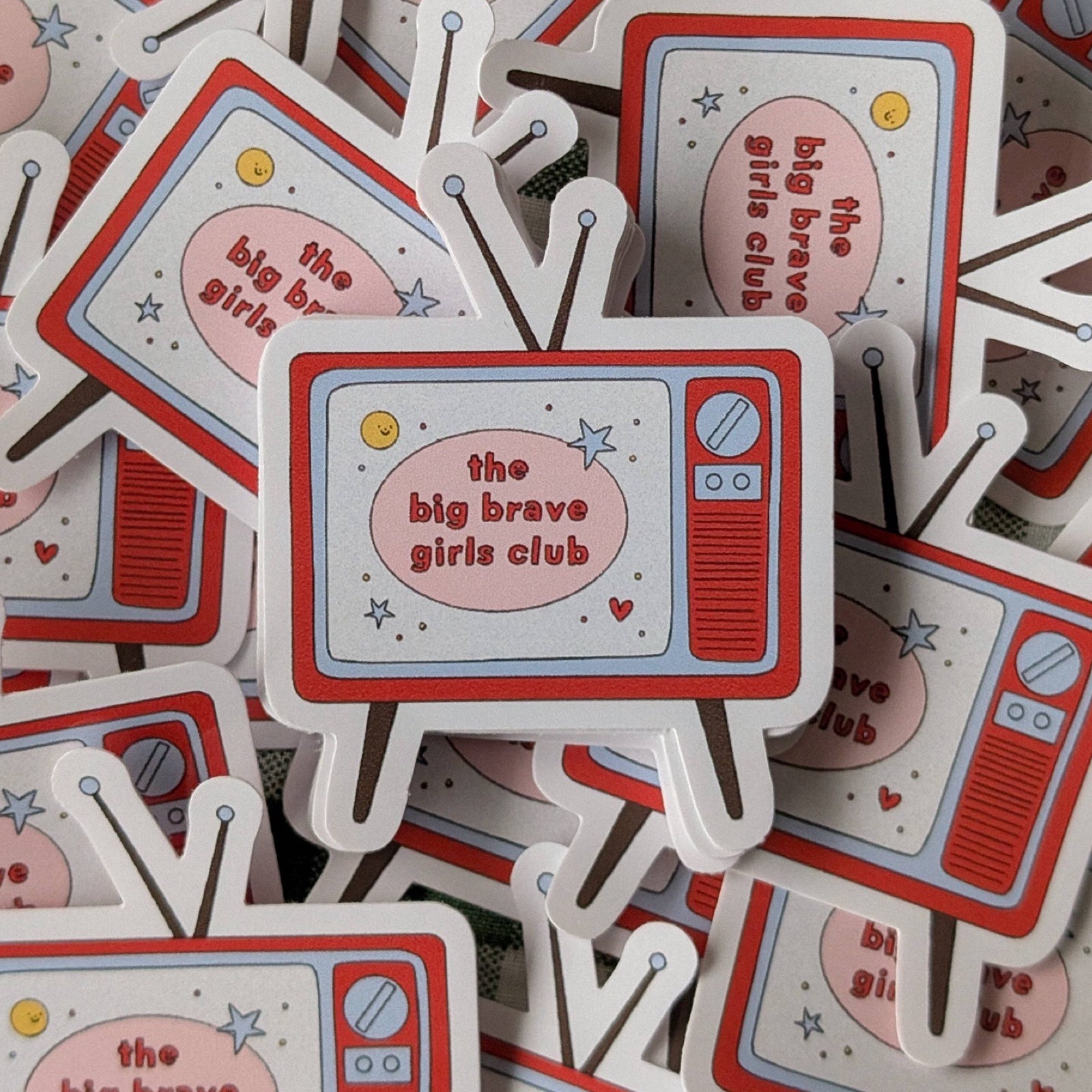 Stickers with 'the big brave girls club' design on a pile of similar stickers.