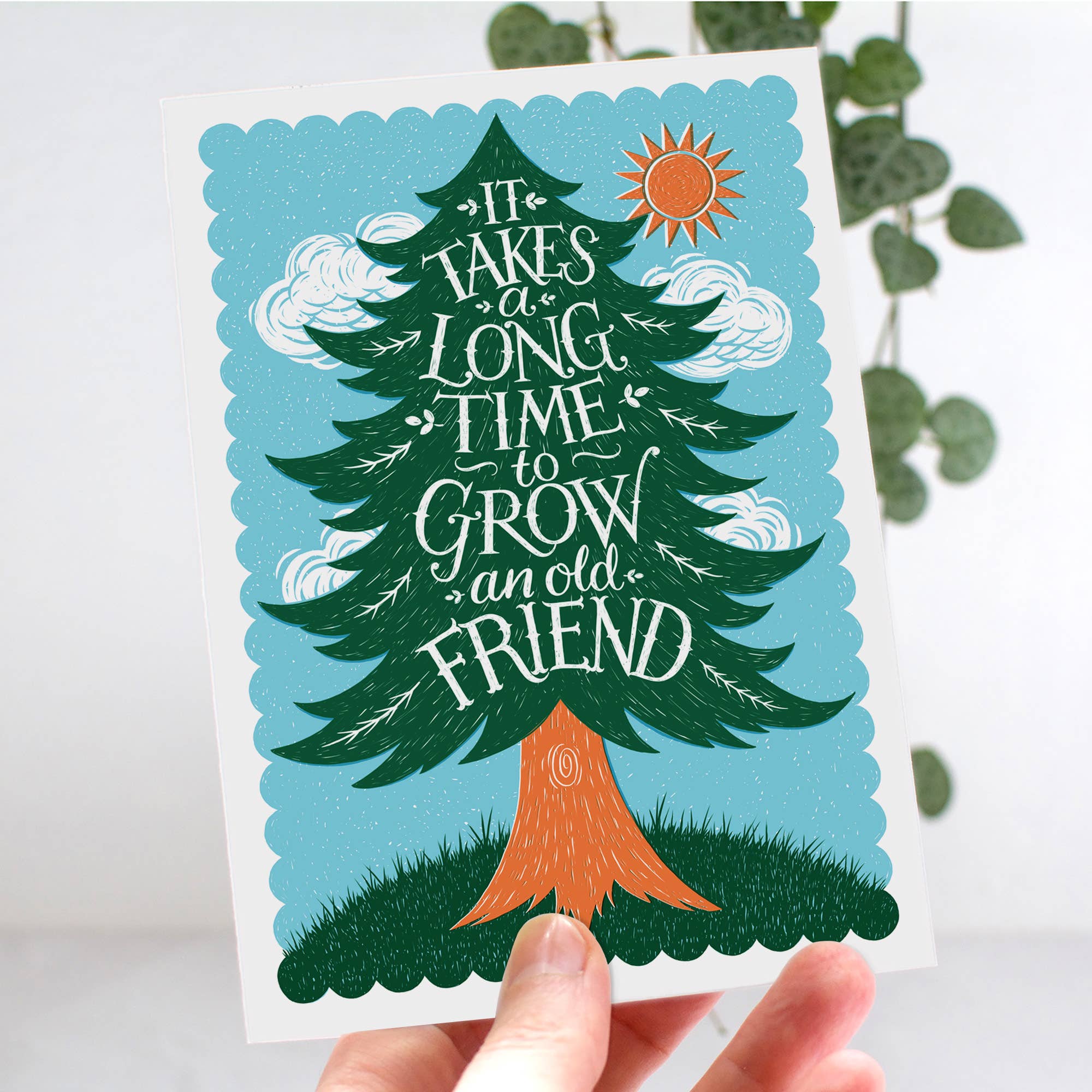 Card with a tree illustration and text 'It takes a long time to grow an old friend' held by a hand.