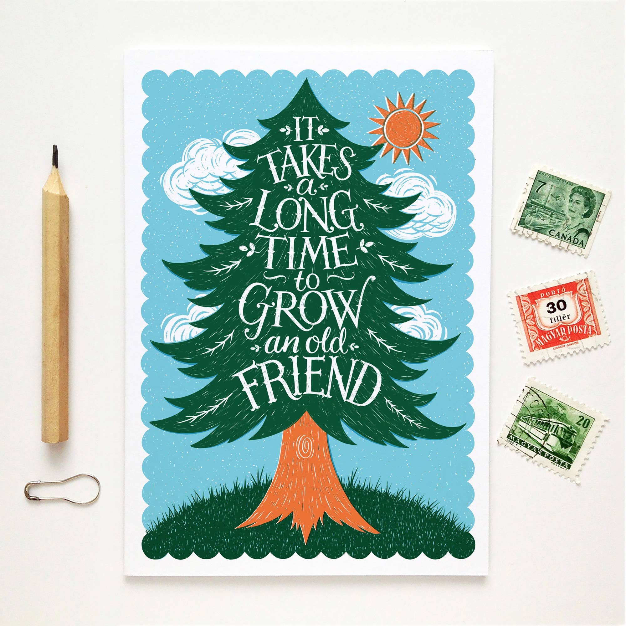 Illustration of a tree with text 'It takes a long time to grow an old friend' on a blue background, with stamps and a pencil on a white surface.