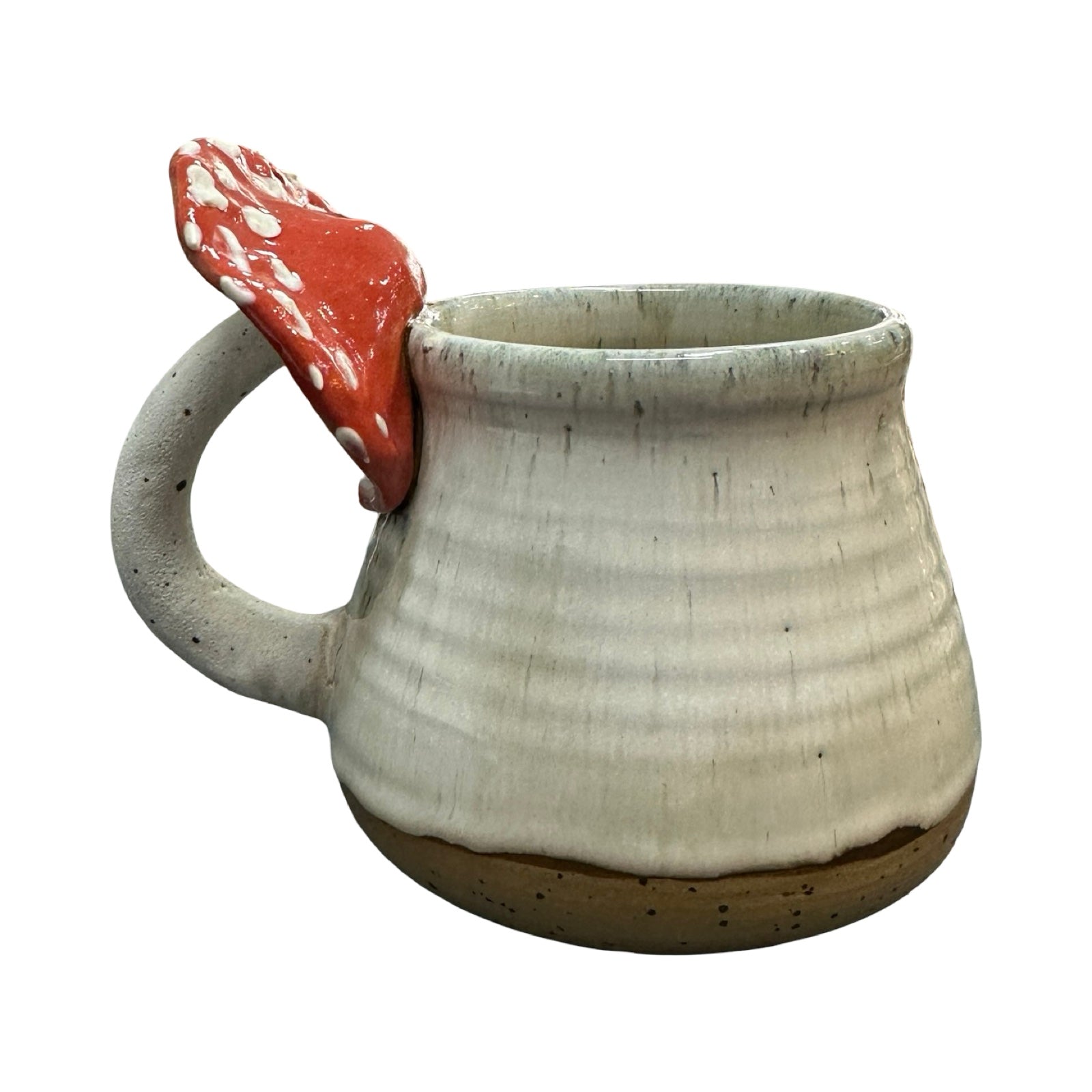 Ceramic mug with a red and white mushroom attached to the handle on a white background.