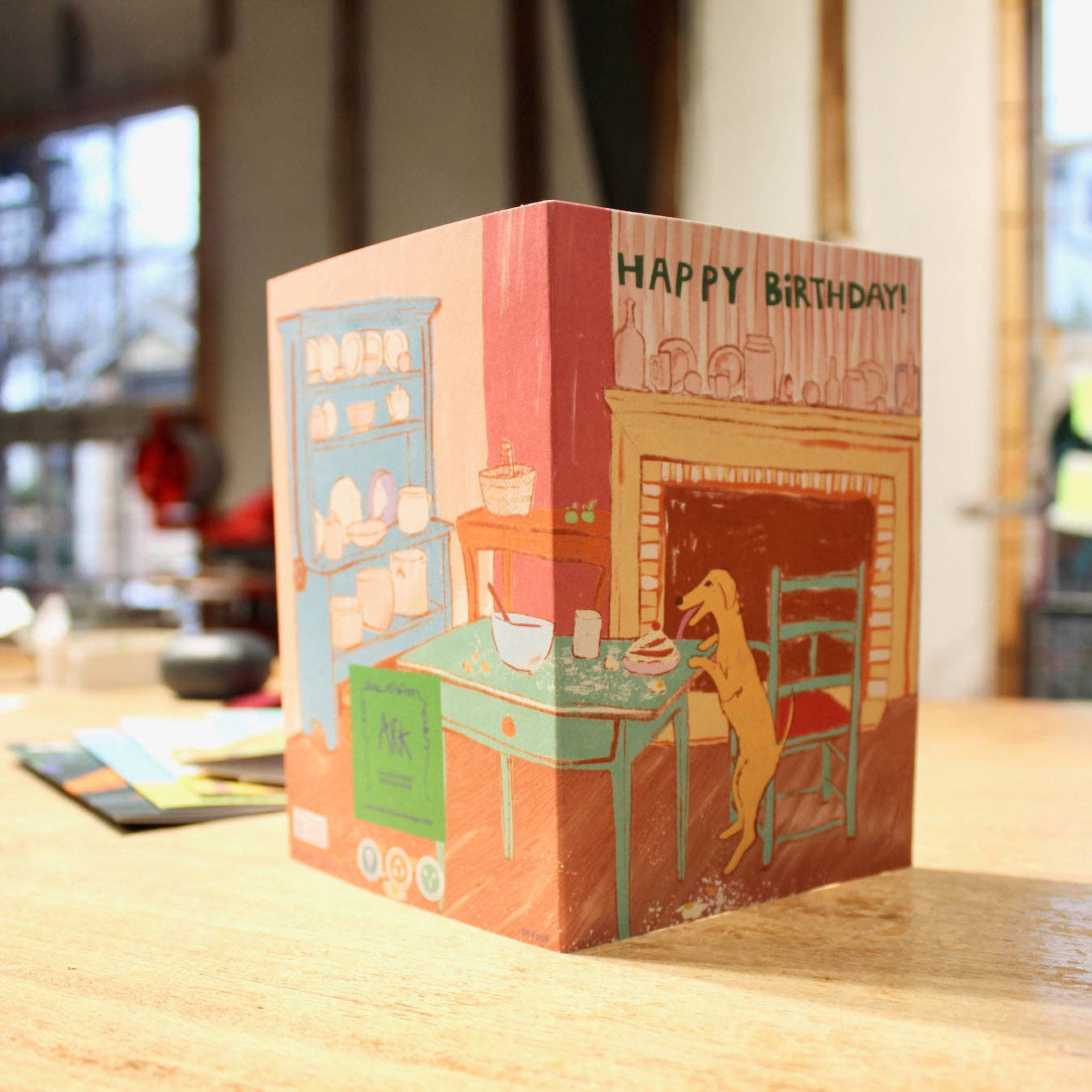 Illustrated birthday card on a wooden surface with a blurred indoor background.