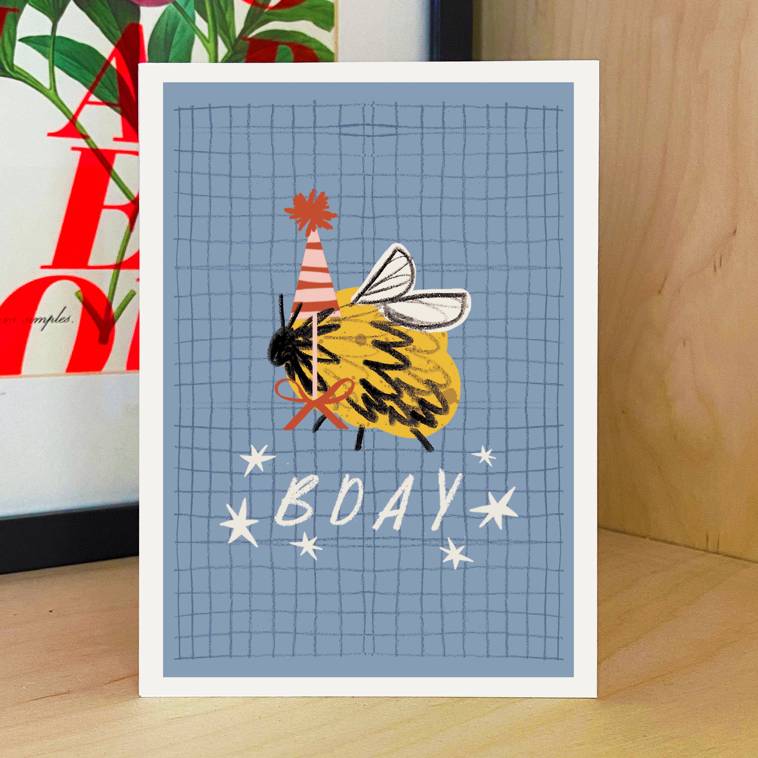 Birthday card with a bee wearing a party hat on a blue grid background.