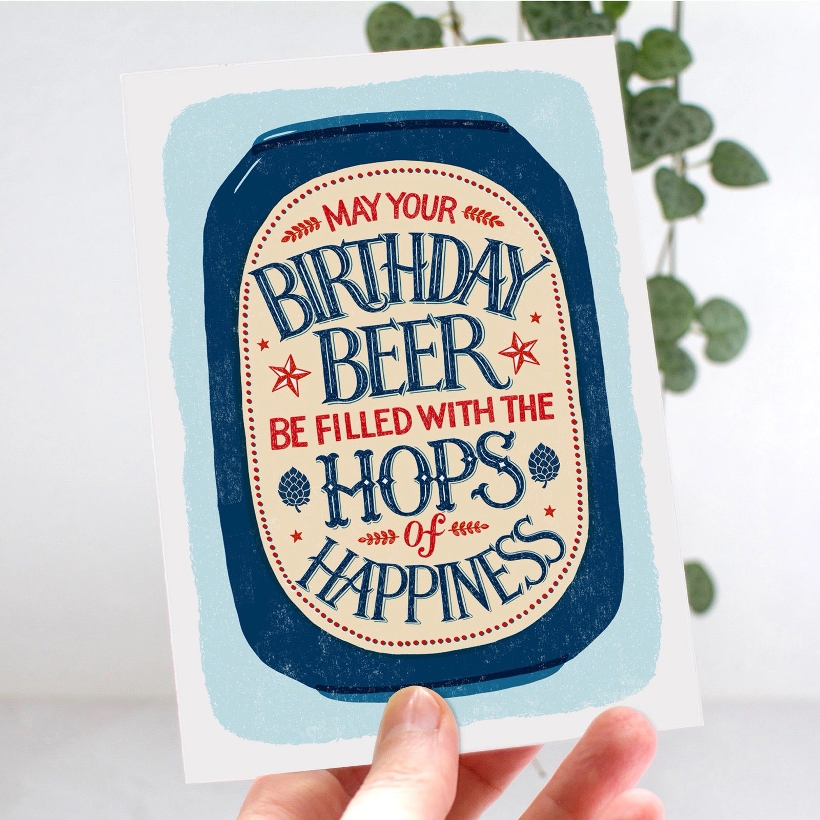Greeting card with 'Birthday Beer' text held by a hand against a light background.