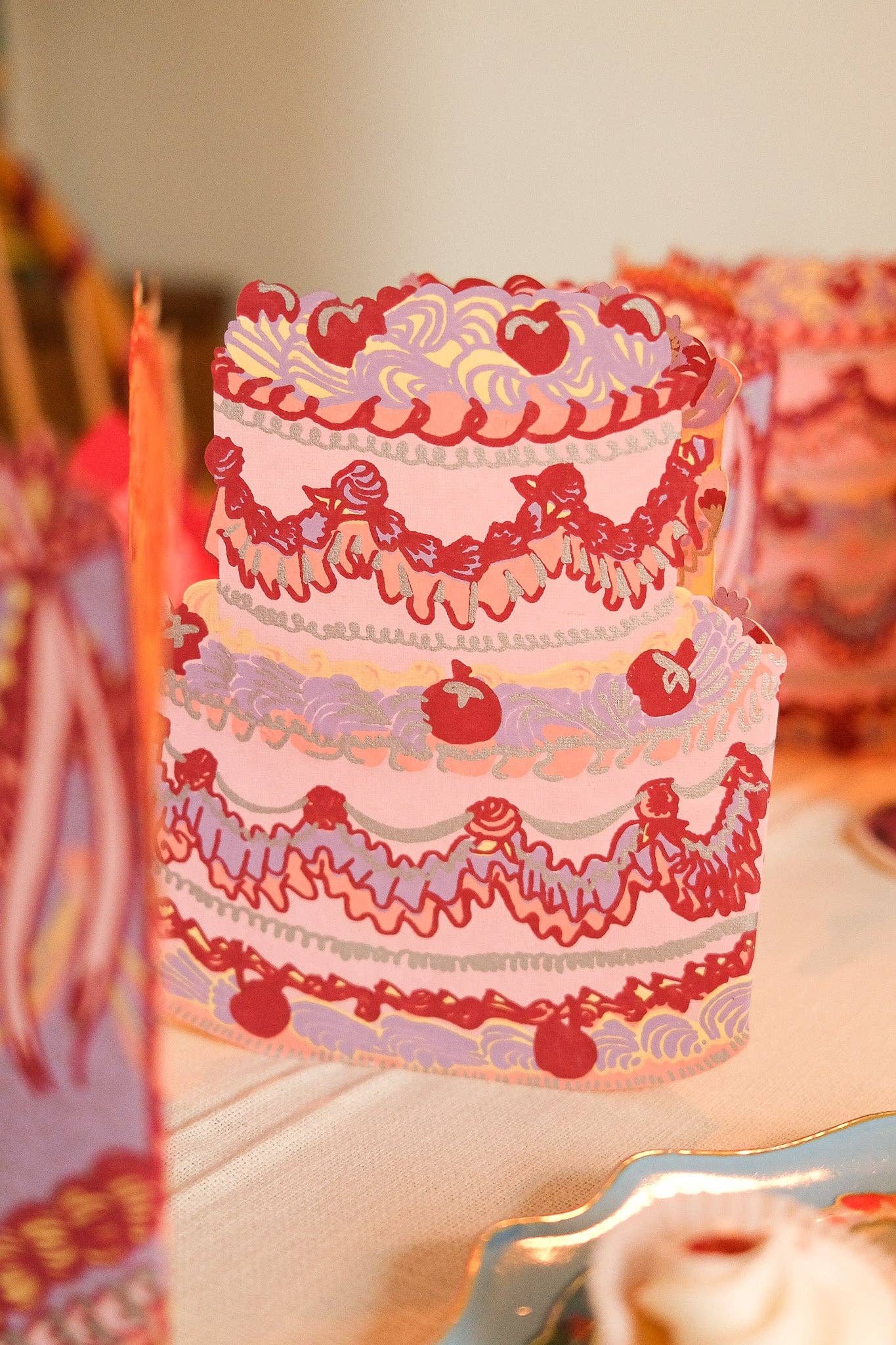 Three-tiered cake with red and white floral patterns on a blurred background.