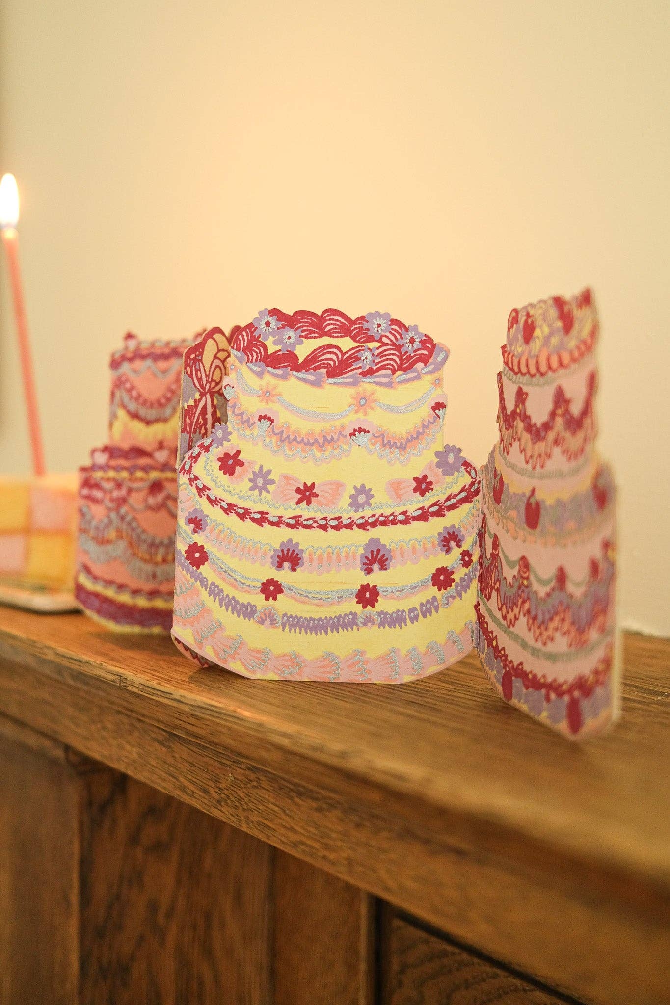 Decorative cake card on a wooden surface with a candle in the background.