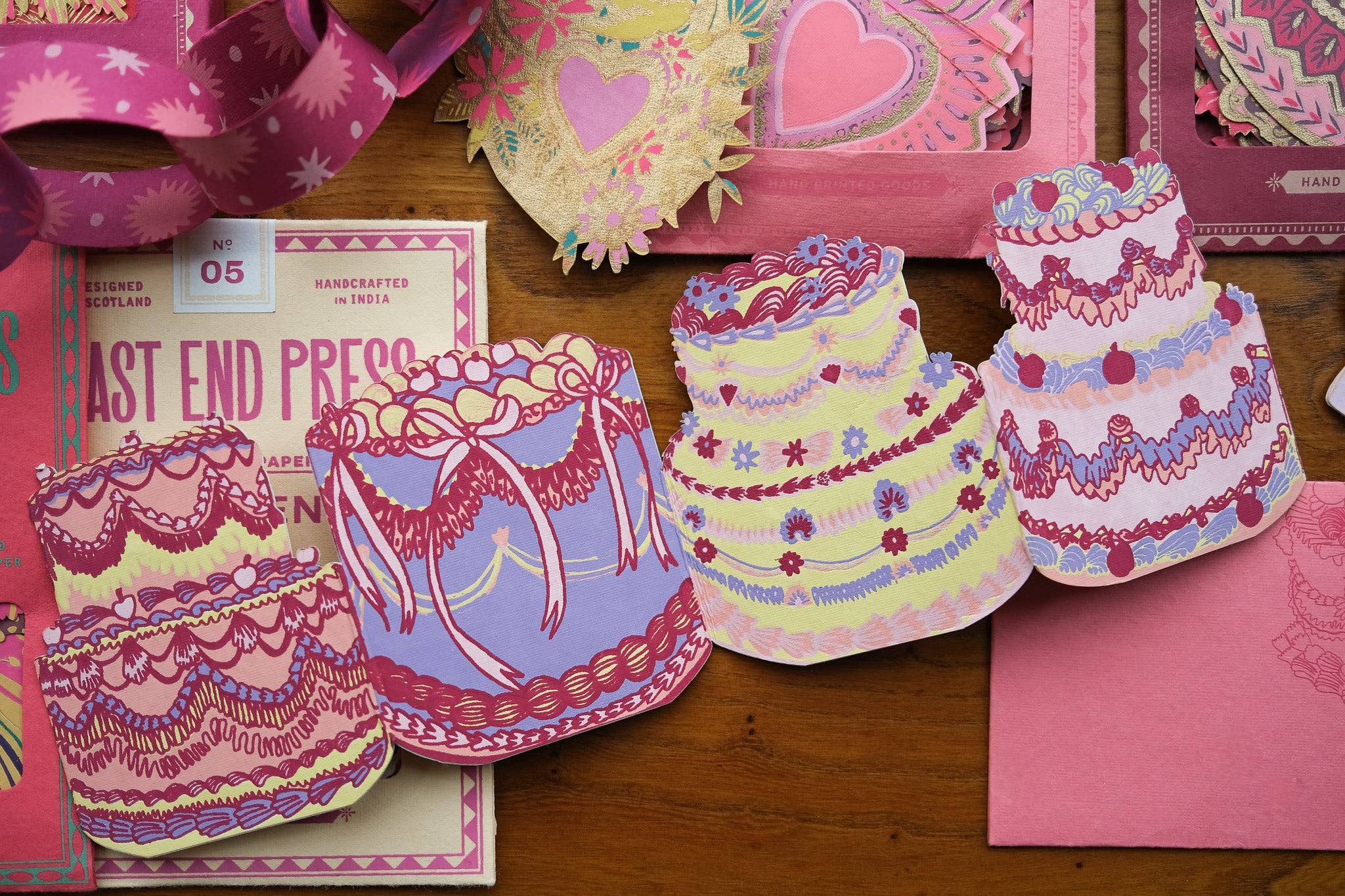 Colourful cake shaped card on a wooden surface with pink packaging.