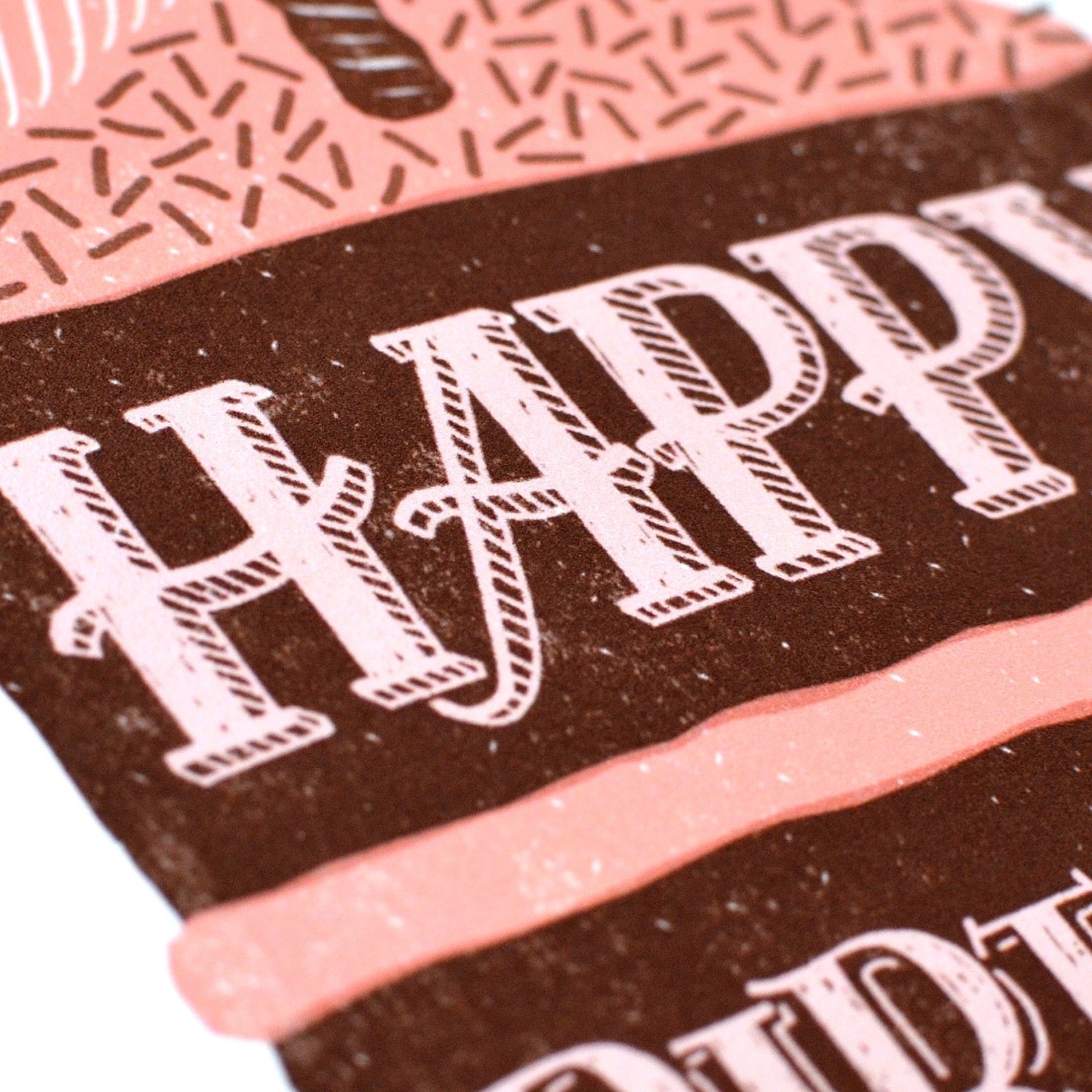 Close-up of a chocolate cake with 'HAPPY BIRTHDAY' text on a pink and brown cake background.