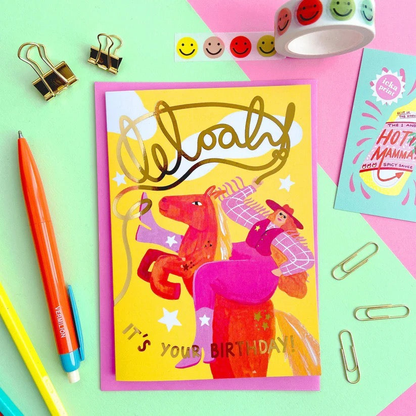 Colourful birthday card with illustration of a person on a horse, surrounded by stationery items on a multicoloured background.