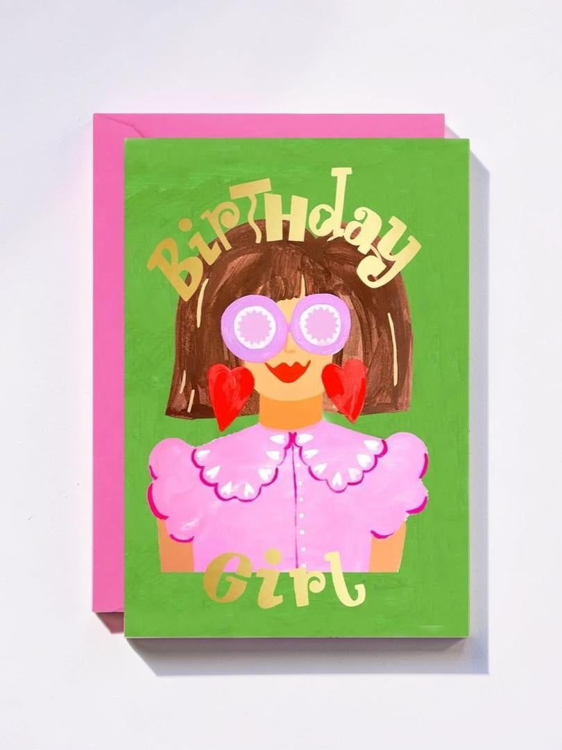 Birthday card with a colorful illustration of a girl wearing glasses and a pink outfit on a green background.