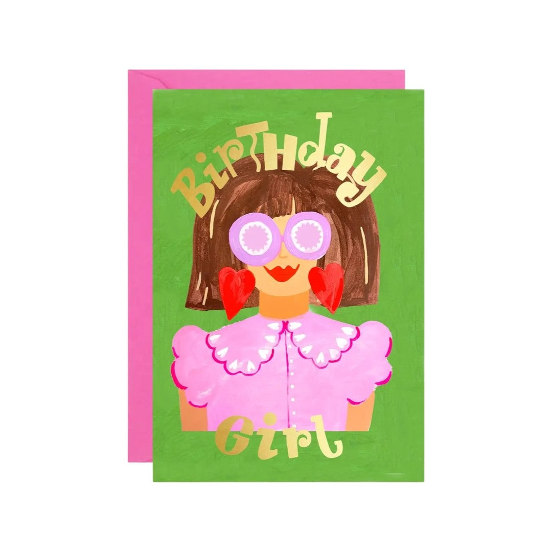 Birthday card featuring an illustration of a brown-haired girl is a pink shirt and pink glasses with fabulous red earrings and the text 'Birthday Girl' in gold, all on a green background.