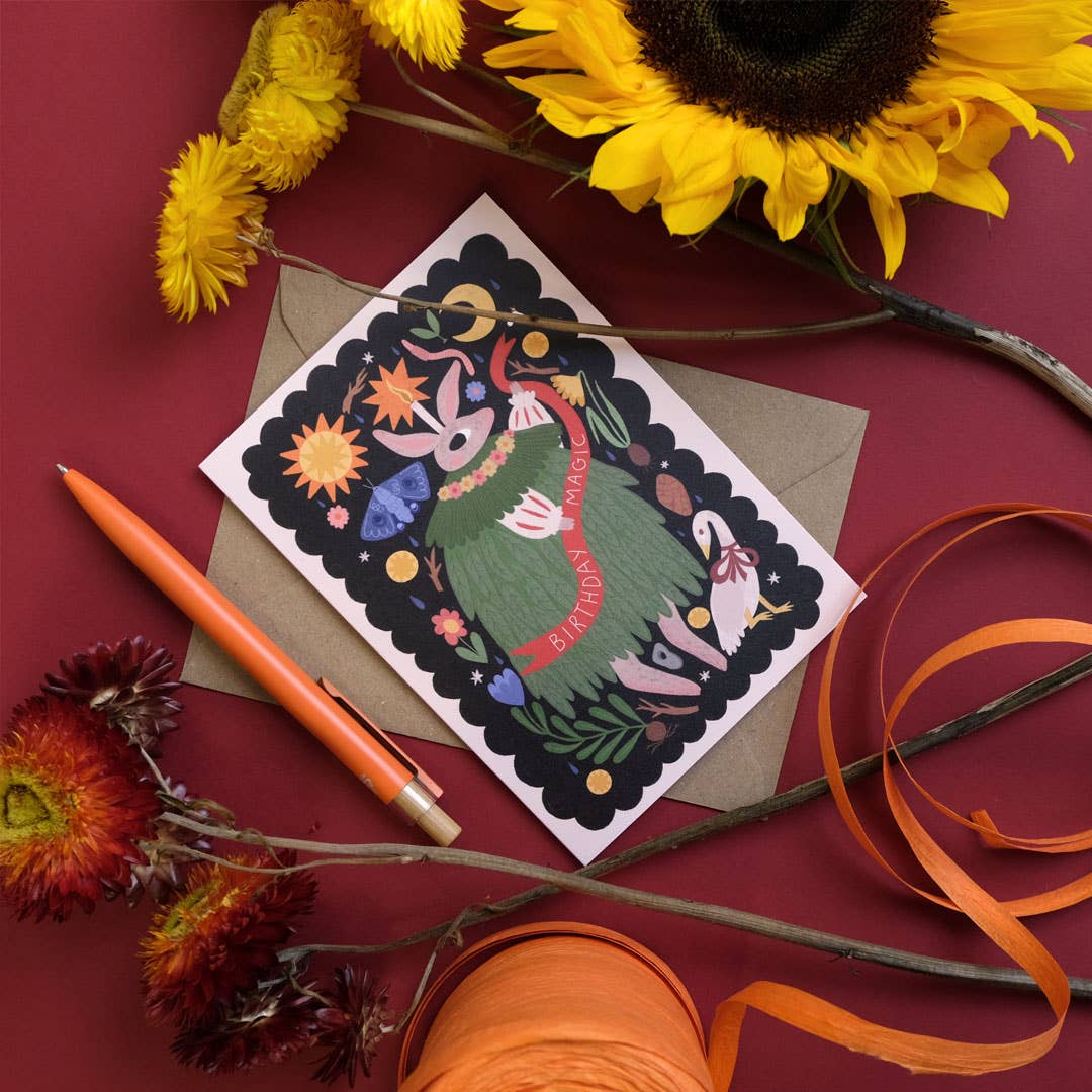 Decorative greeting card with colorful design on a red surface with flowers and a pen.