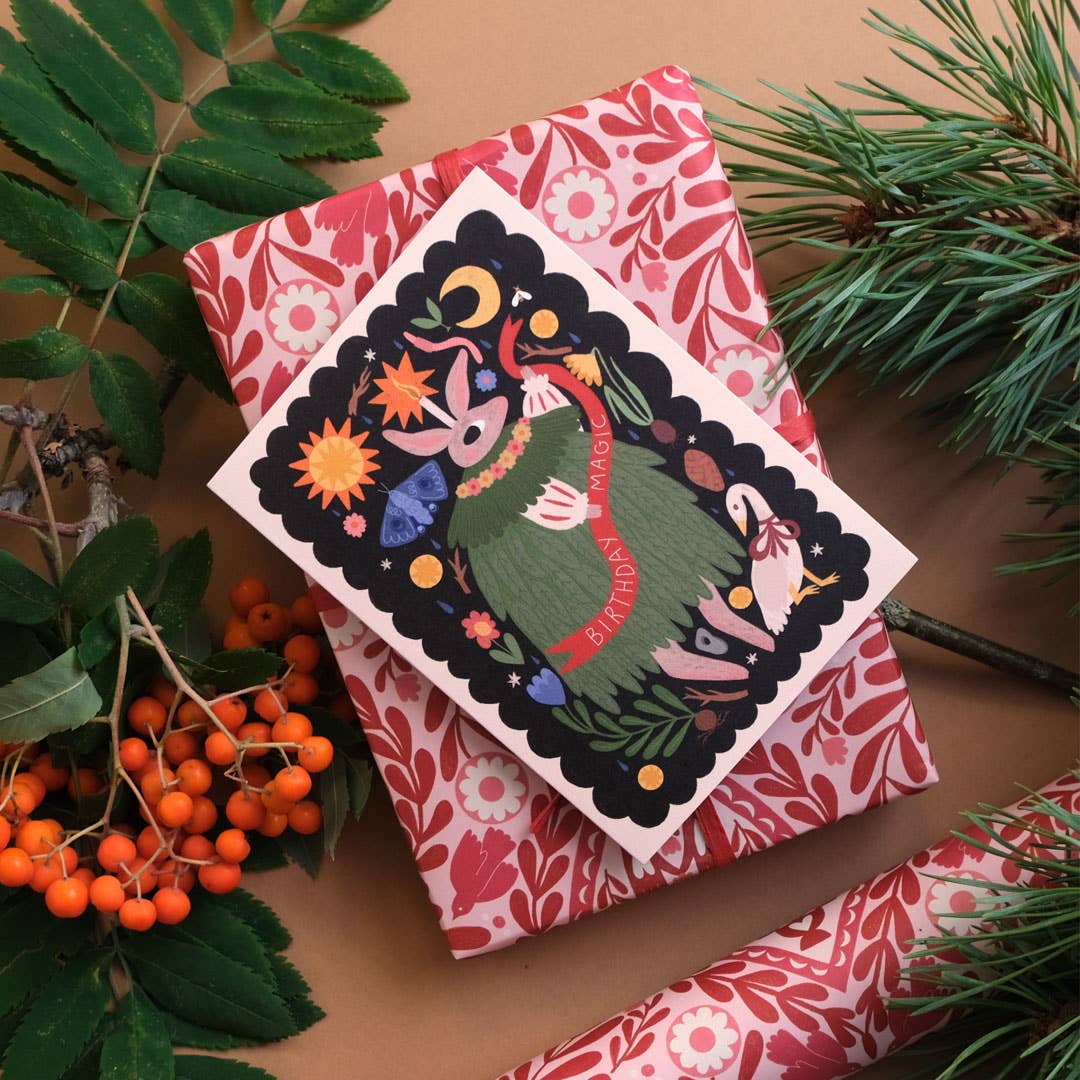 Decorative card with a colorful illustration of a character, surrounded by greenery and berries on a brown surface.