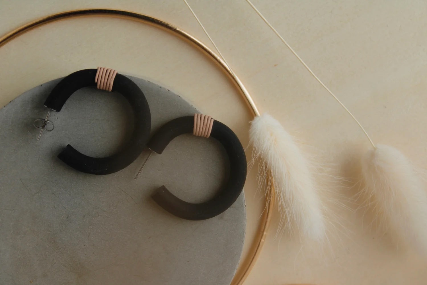 A pair of black wrap hoop earrings with hypoallergenic stainless steel fixings, on a table, next to a plant.