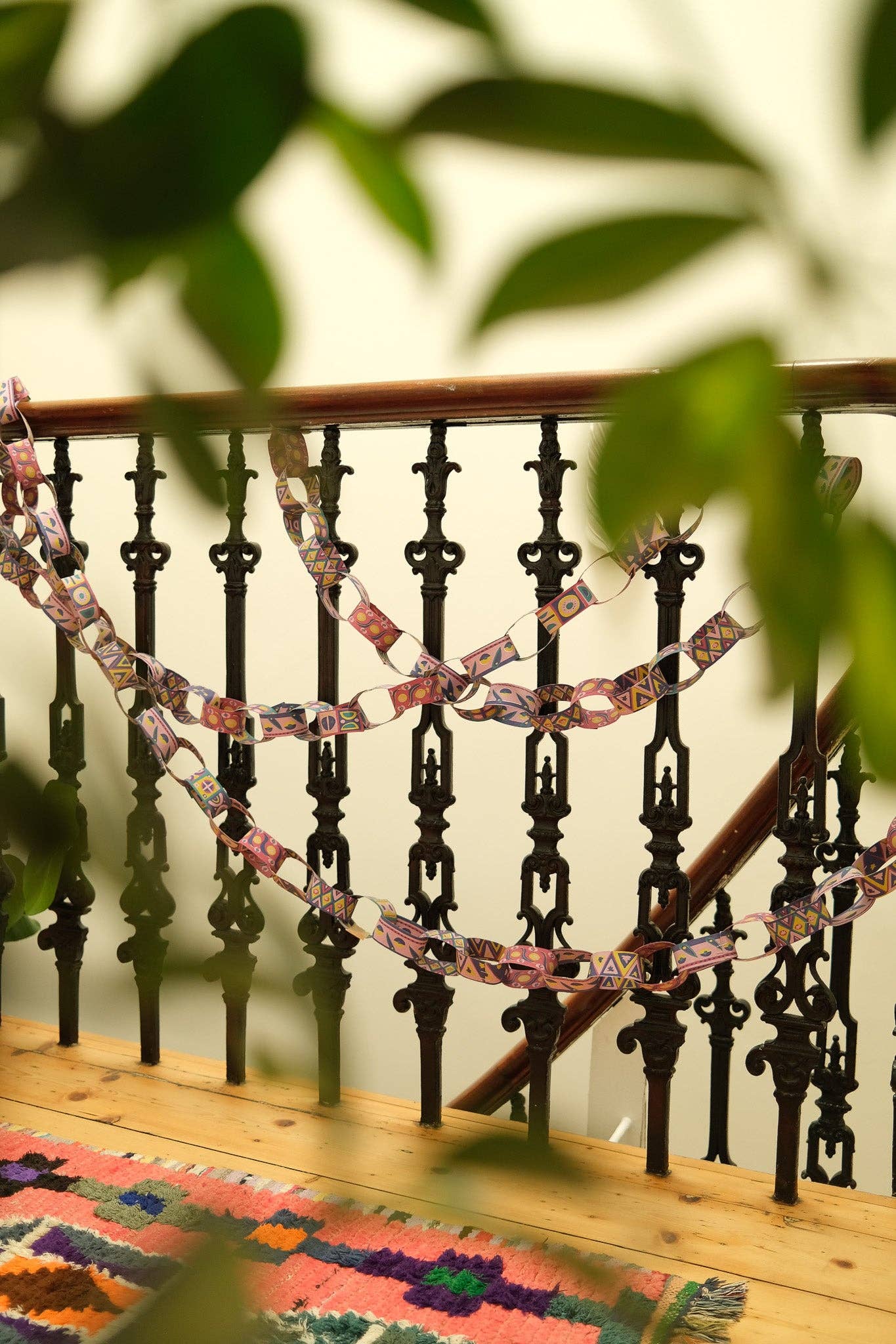 Decorative paper chain on a railing with green leaves in the foreground.