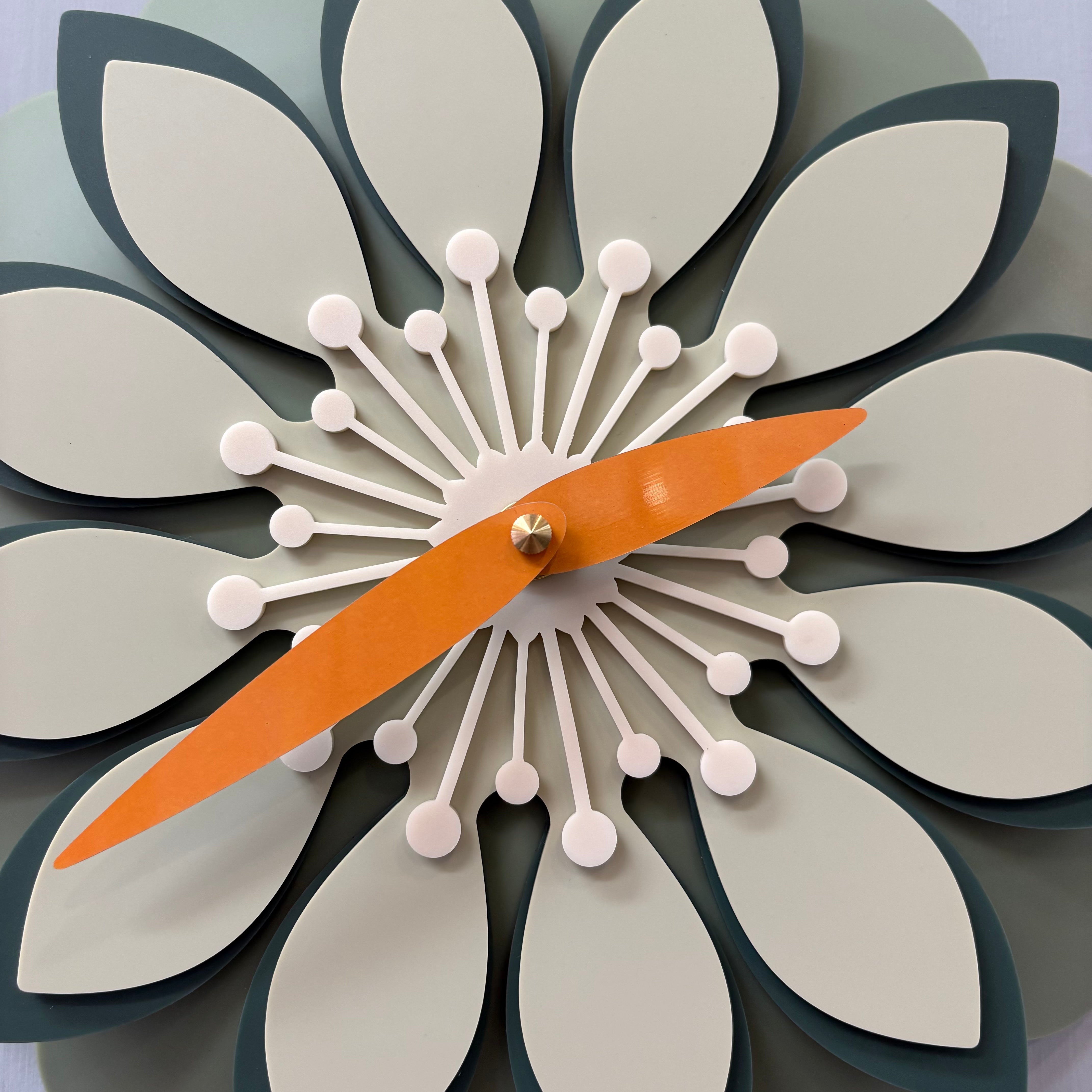 Decorative wall clock with a floral design and orange hands on a light grey background.