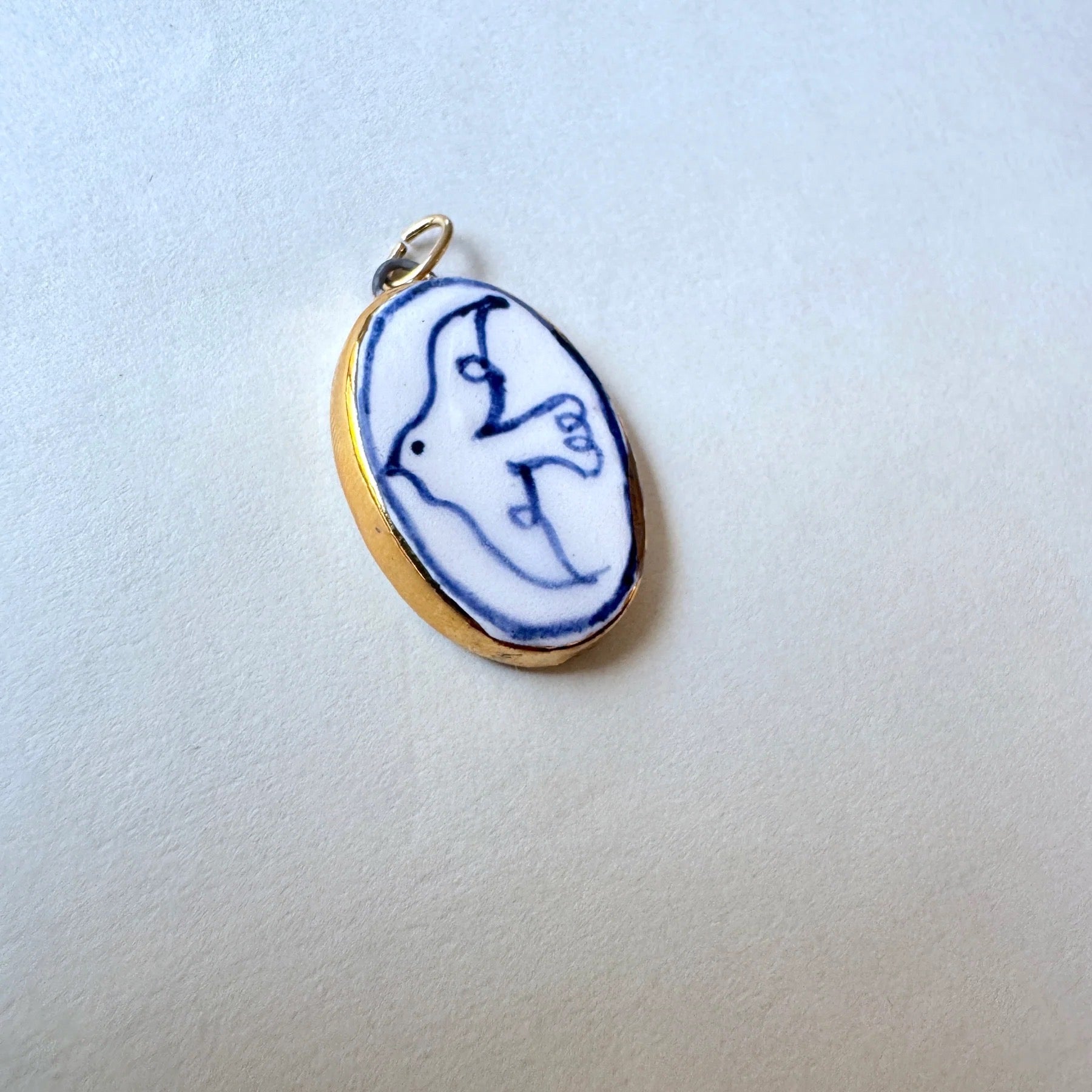 Gold pendant with a blue and white dove on a light grey background.