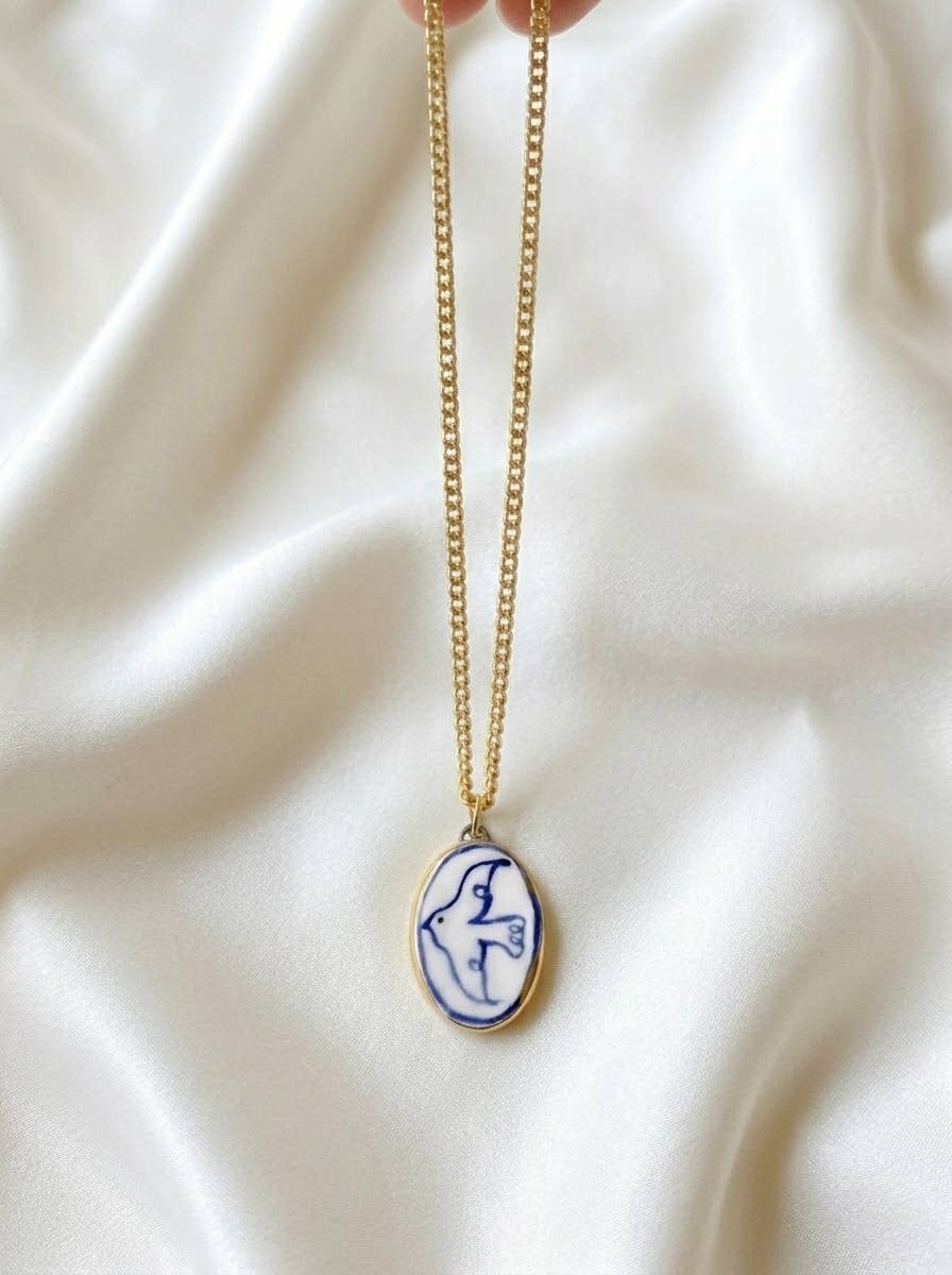 Necklace with a pendant of a blue bird on a white fabric background.