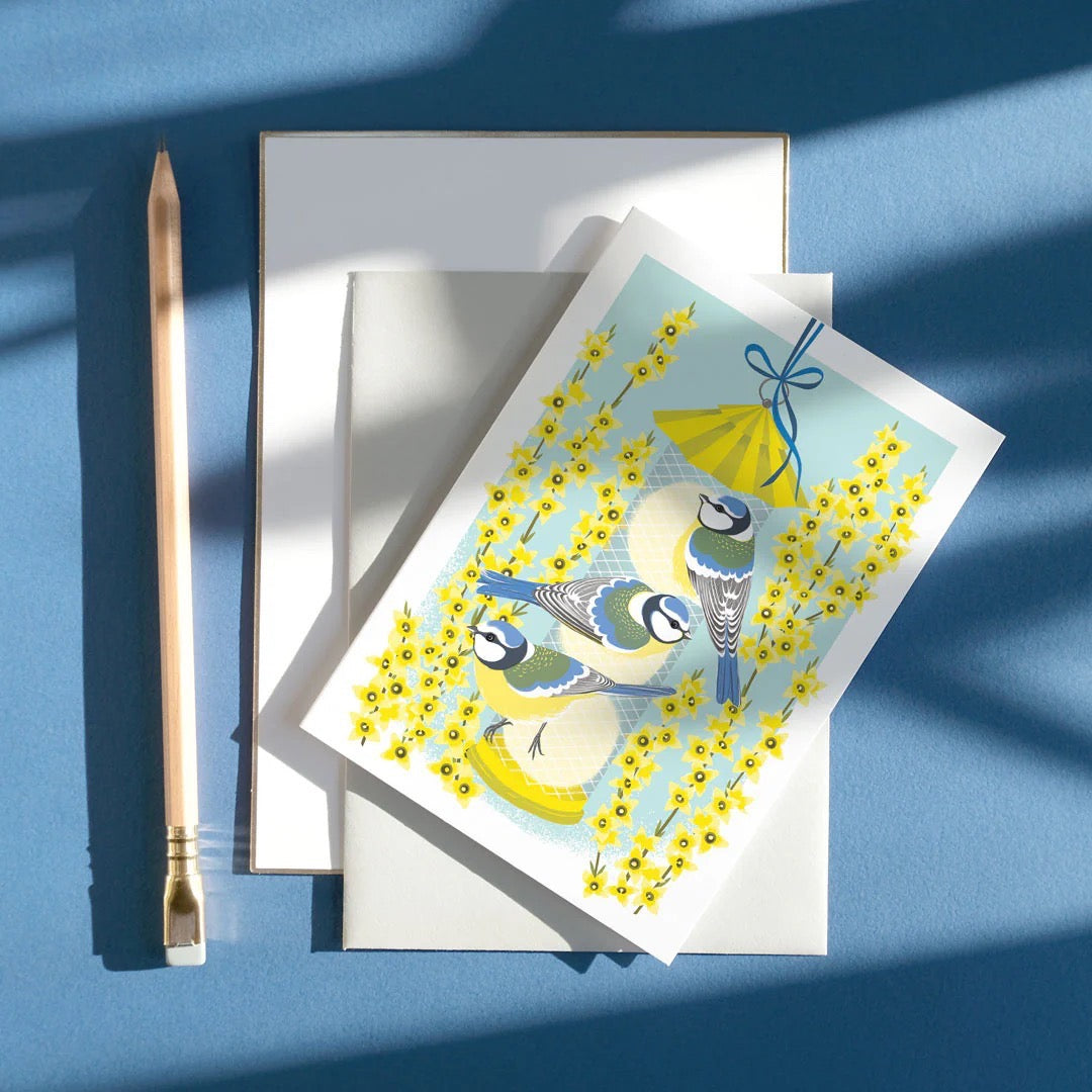 Greeting card with birds and flowers on a blue surface with a pen.