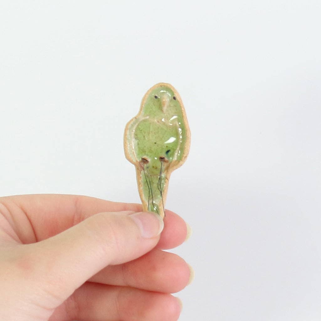 Hand holding a small ceramic bird figurine against a white background.