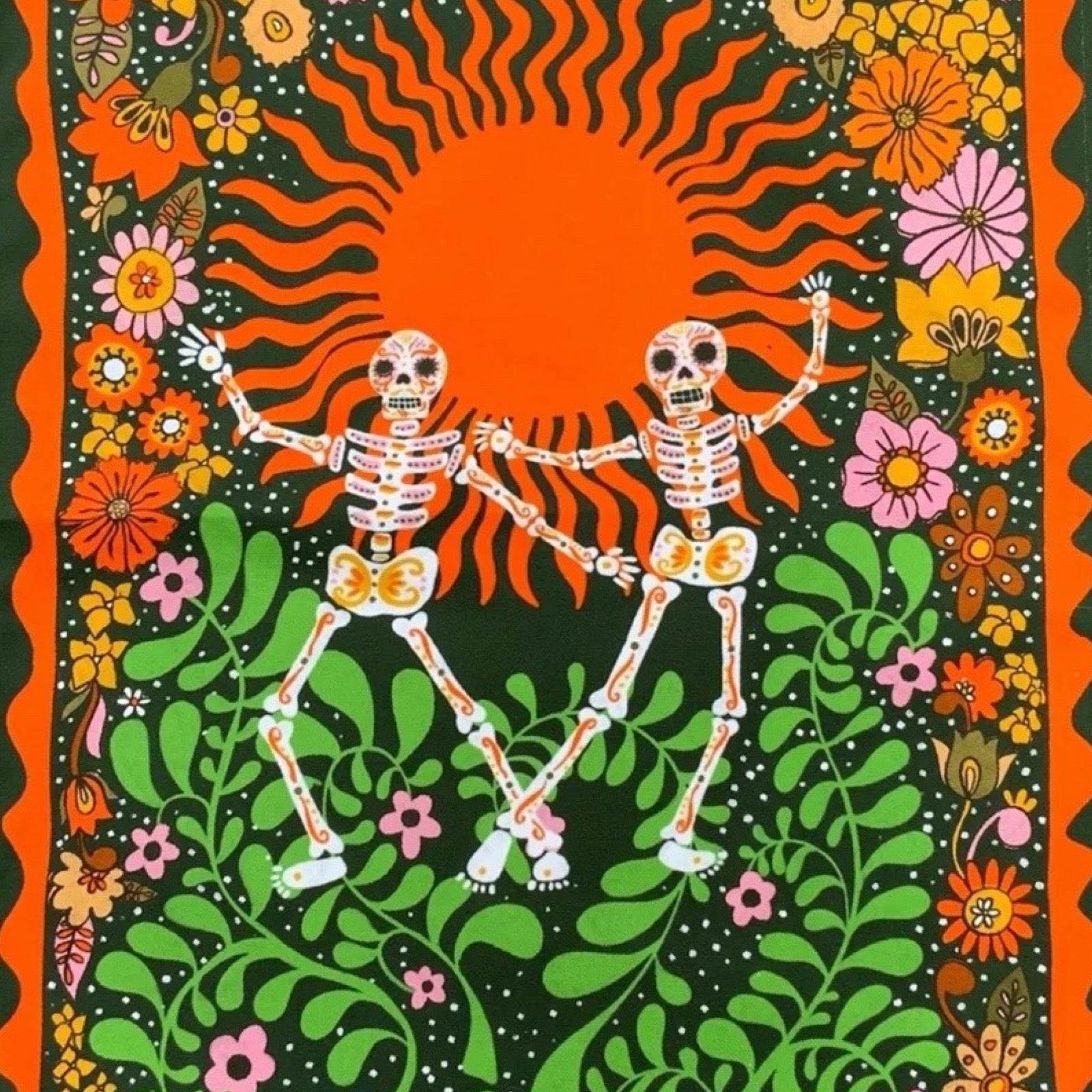 A statement tea towel featuring skeletons dancing on a green and orange background, with multicoloured flowers and skulls.