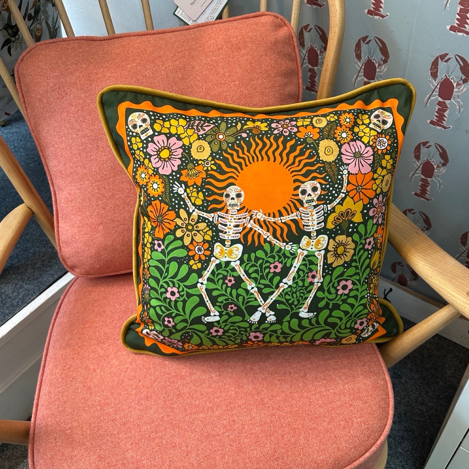 Decorative cushion with skeletons and floral patterns on a pink chair.